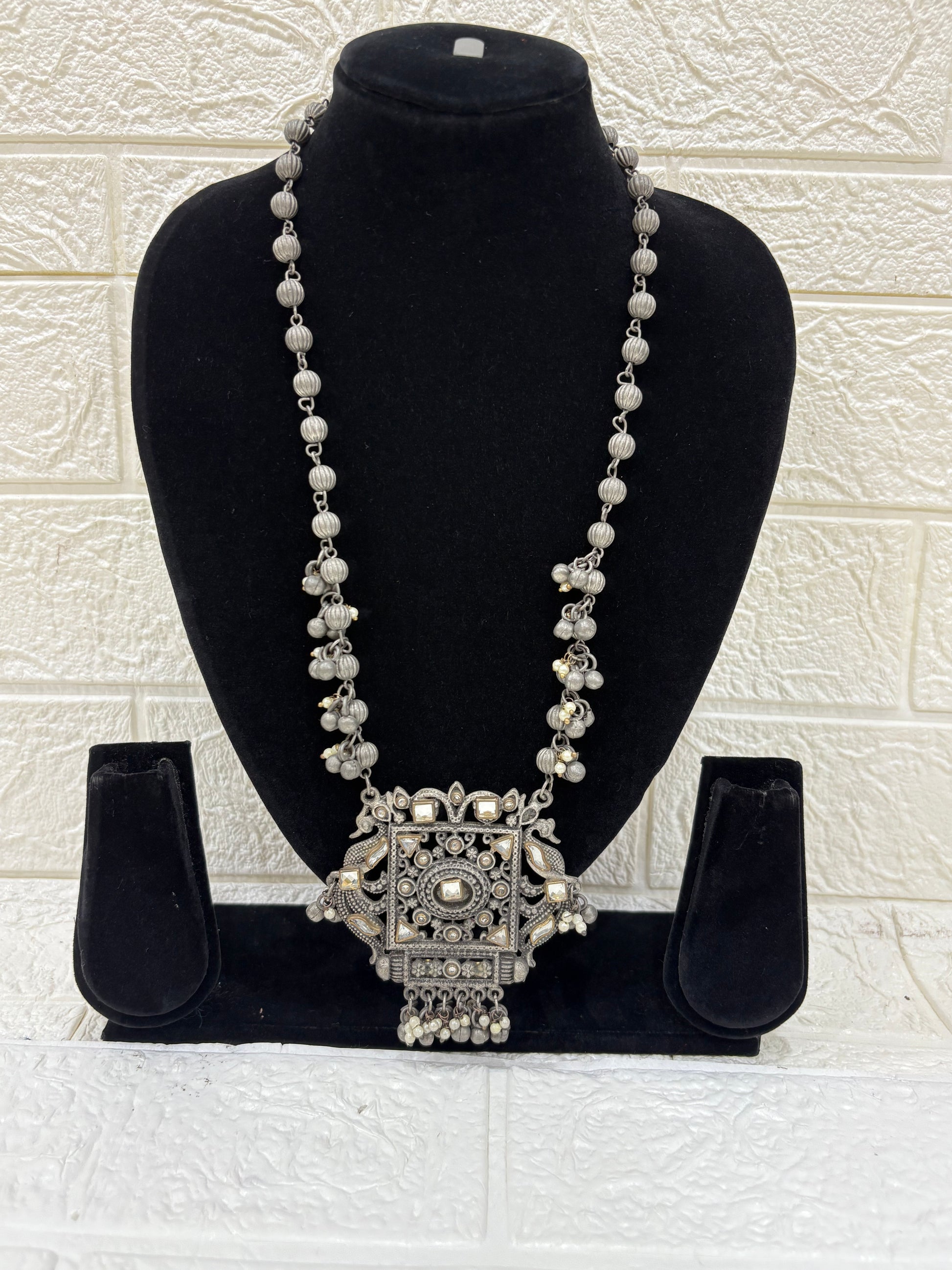 Name:
Antique Mirror Pendant Necklace Traditional oxidised silver necklace featuring a bold square mirror pendant with intricate detailing and dangling ghungroo accents for a statement festive look.