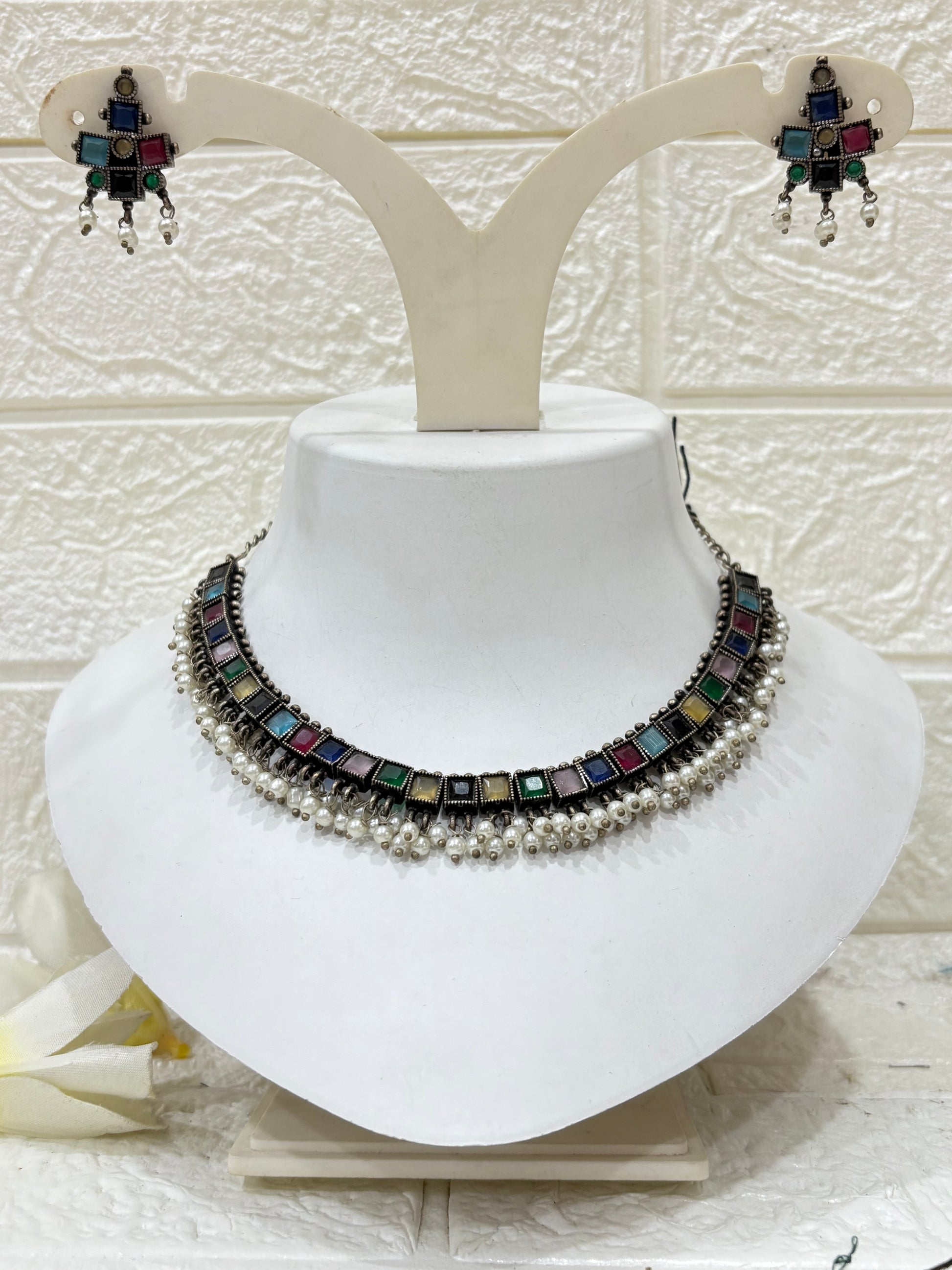 NAME: Boho Mirror Pearl Choker Set Oxidised silver choker adorned with multicolour square stones and pearl drops, paired with matching earrings. Ideal for festive and traditional looks.