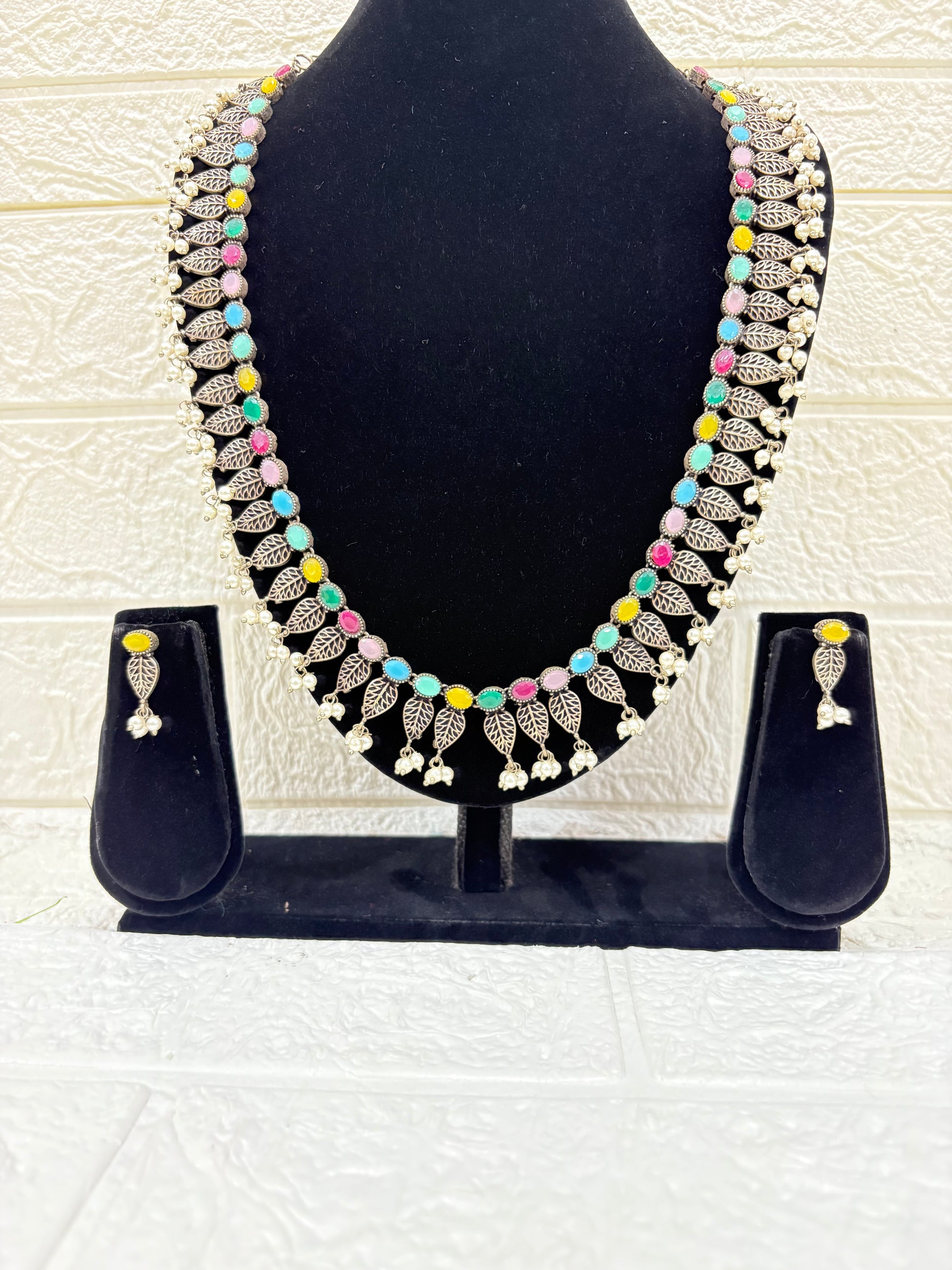 Name:
Colorful Stone Leaf Necklace Set Elegant oxidised silver necklace with multicolor stones, leaf motifs, and pearl drops, paired with matching earrings for a festive ethnic look.