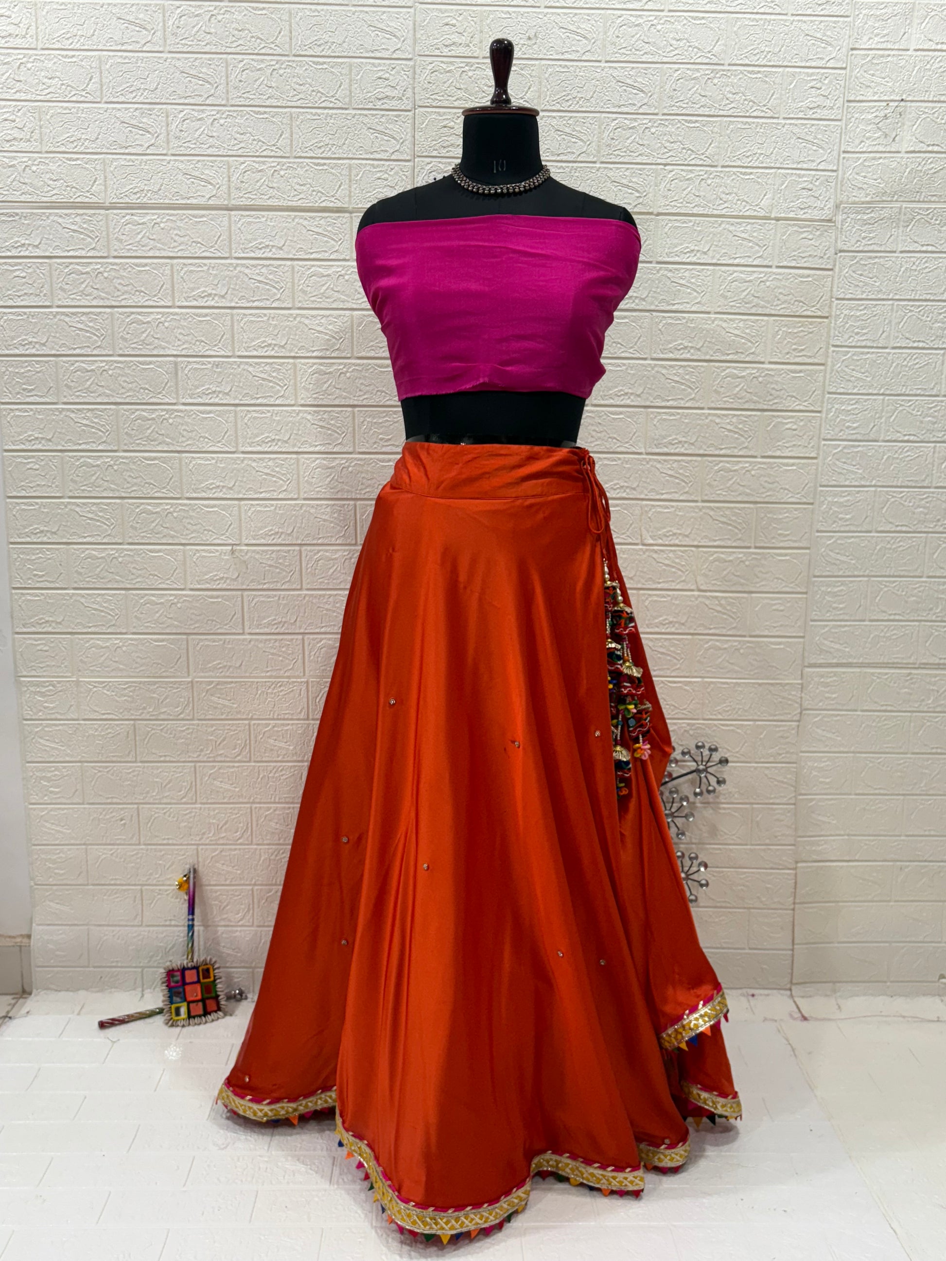 Name: Rust Orange Festive Lehenga Set Crafted soft satin blend with a cotton silk contrast pink blouse and chiffon dupatta, embellished with delicate lace border and subtle mirror work – perfect for festive occasions.