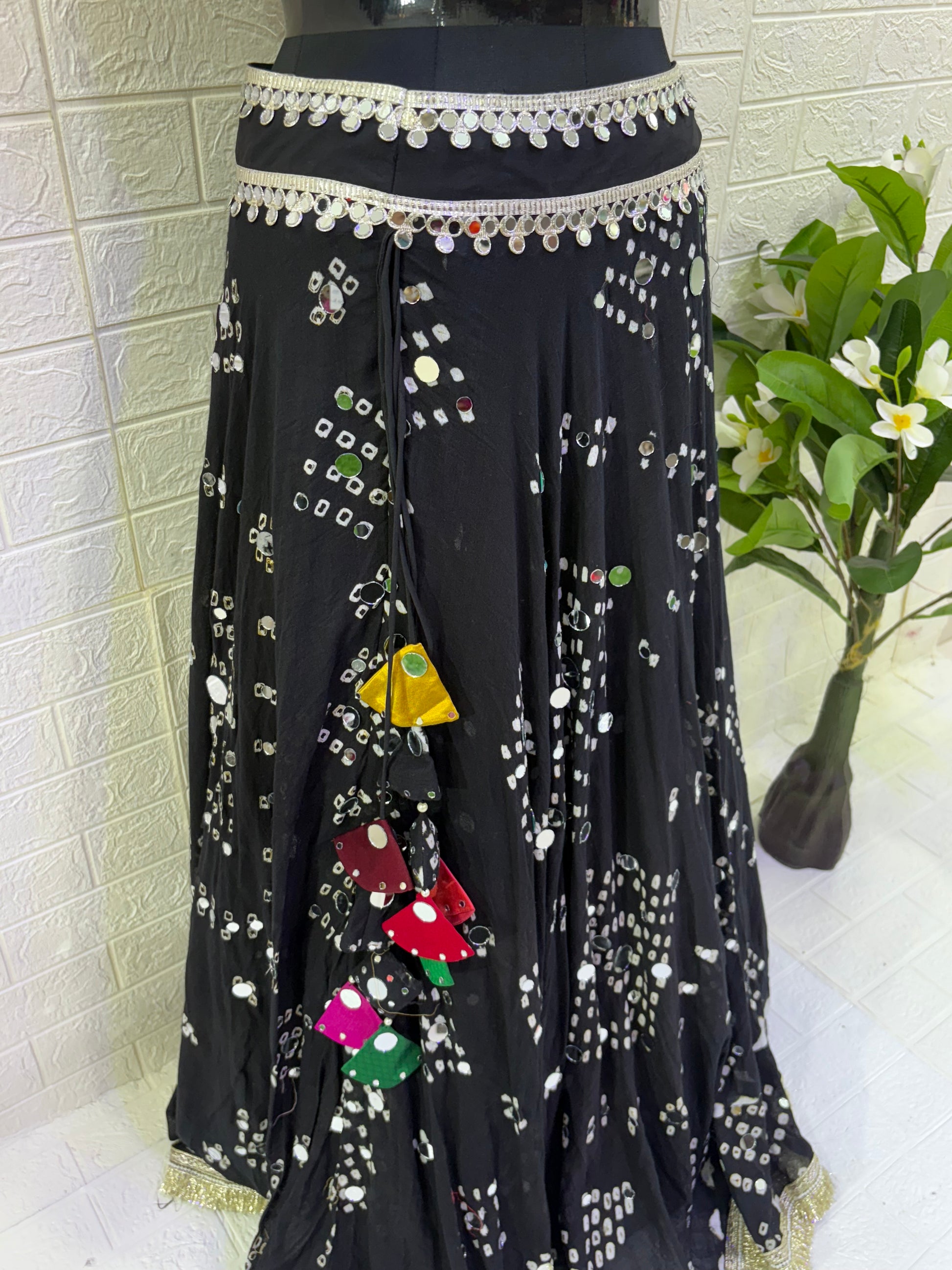 Name:
Midnight Mirror Bandhani Lehenga Elegant black cotton bandhani lehenga with mirror work and colorful tassels, paired with a tribal-inspired Ajrakh blouse for a bold festive vibe.