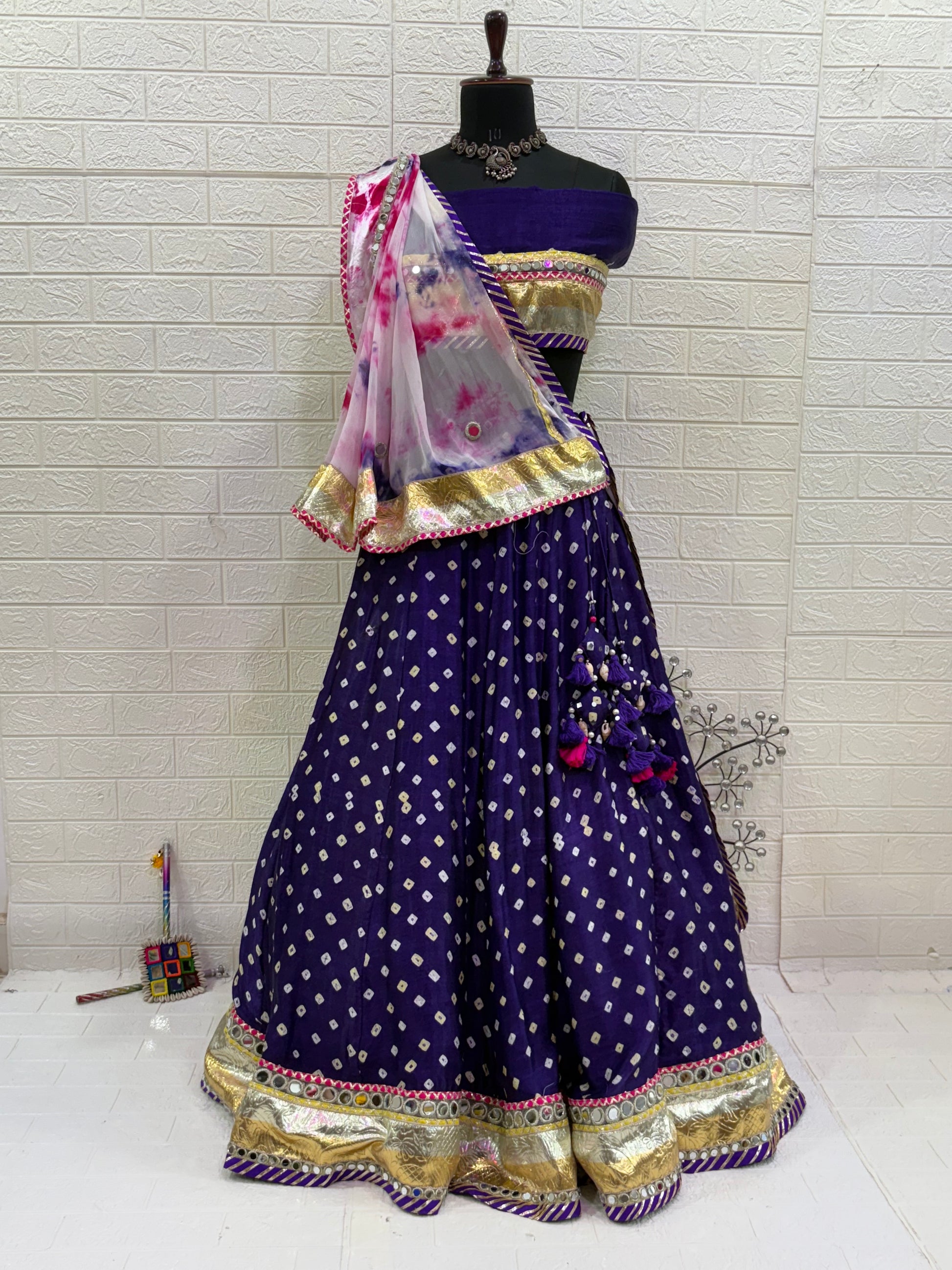 Name:
Royal Purple Bandhani Lehenga Set Made from soft synthetic satin Bandhni print with traditional paired with a contrast tie-dye dupatta and golden lace and long lumpy lace detailing for a vibrant festive look.