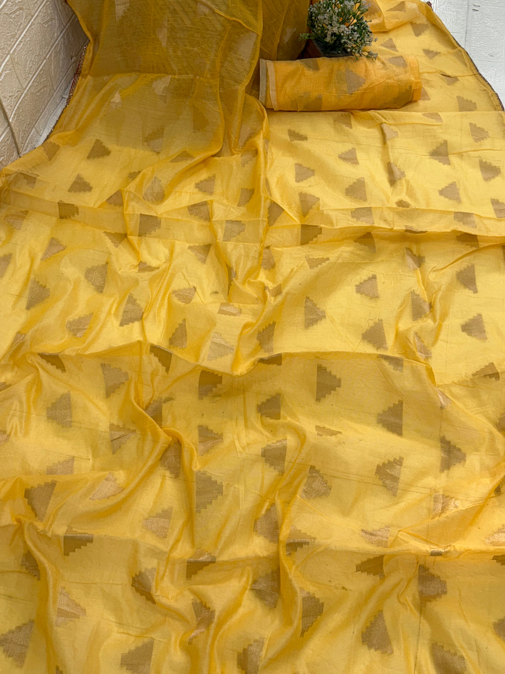 The saree is most likely cotton silk a blend like  The lightweight, sheer nature of the yellow fabric, adorned with all-over gold zari woven triangular motifs, is characteristic of these silks. The geometric patte