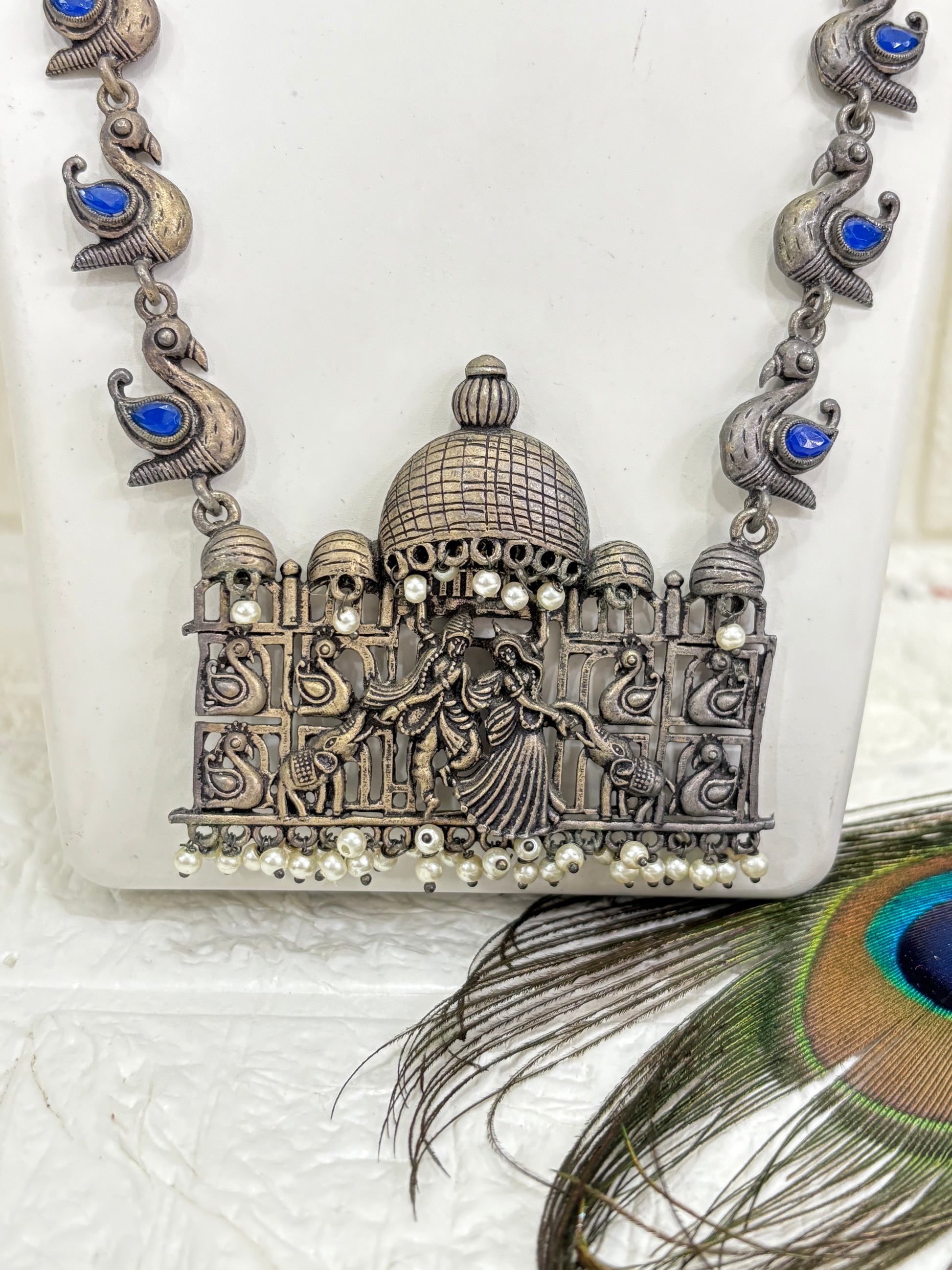 Name:
Heritage Dandiya Dome Necklace Set Oxidised silver necklace with temple-style dome pendant featuring dandiya dance motifs, accented with blue stone paisleys and matching jhumka earrings.
