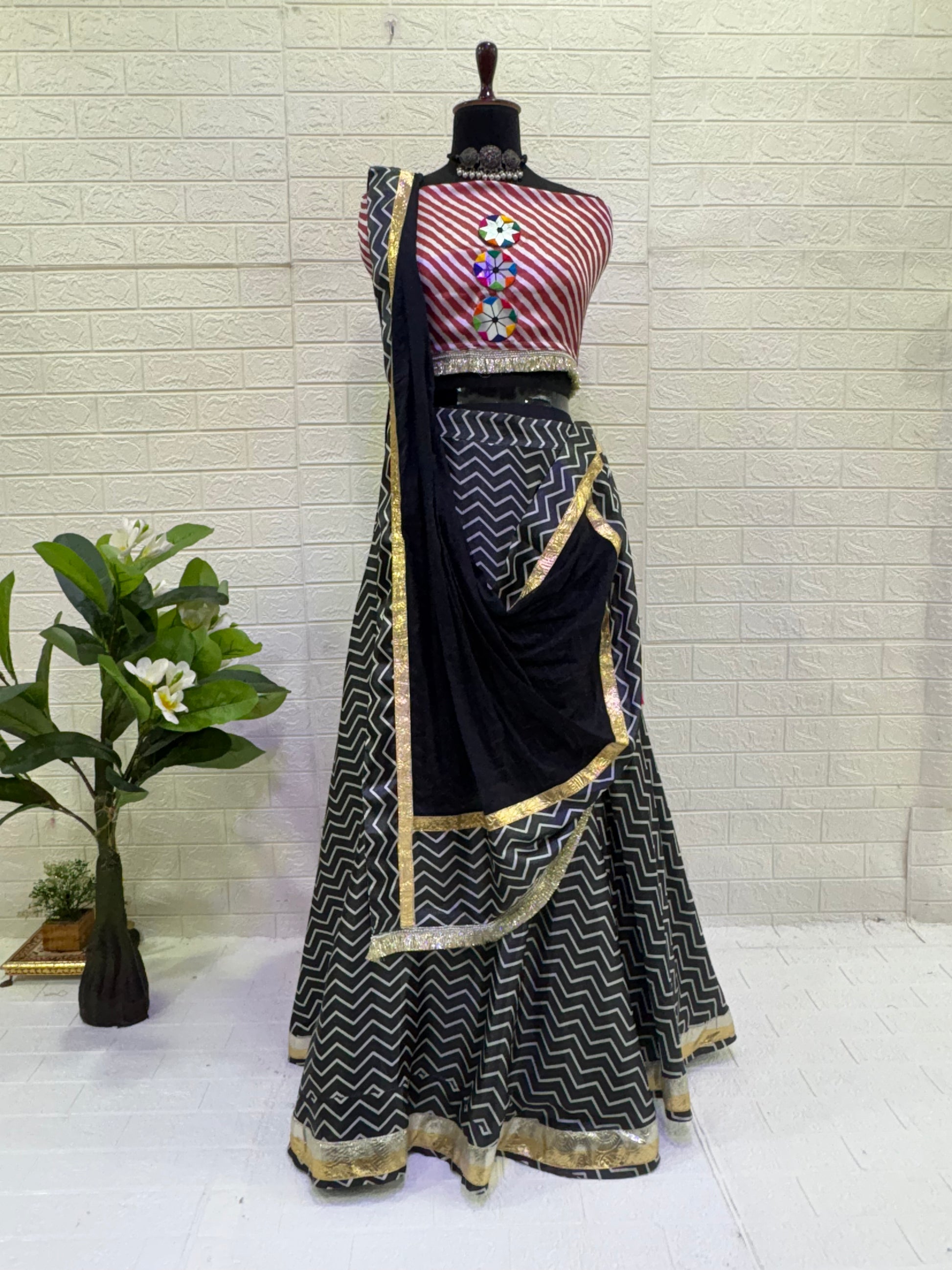 Name: Black & Red Chevron Lehenga set Crafted from soft satin blend with bold chevron print vibrant multicolor tassels, and mirror detailing with mirror work blouse, and black dupatta with gold border – a chic pick for festive and Navratri celebrations.