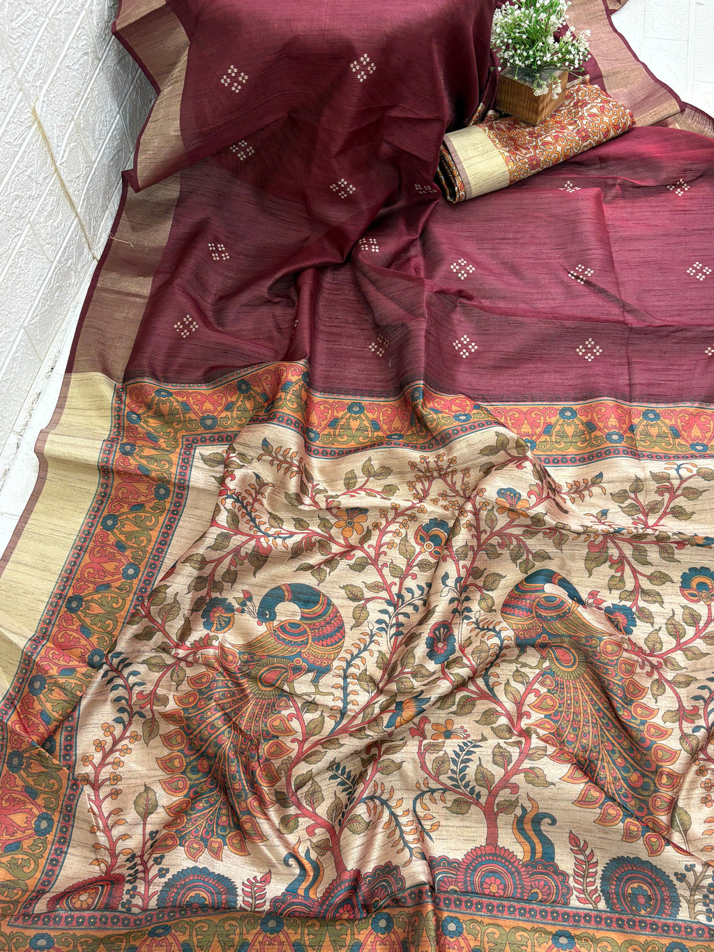 Fabric: Likely Art Silk, The body has a slub/raw silk texture (Maroon/Burgundy), and the pallu features a detailed, nature-inspired design with peacock motifs, which is characteristic of Kalamkari art.