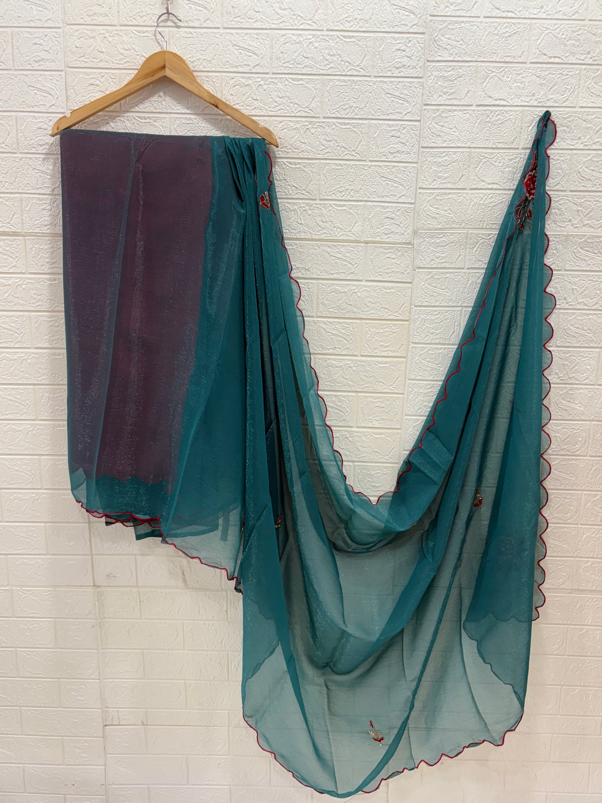 lightweight Teal Shimmer Organza with Embroidered material in a teal shade. It has a sheer, slightly shimmery texture with delicate embroidered floral motifs in red and gold scattered across the fabric. The border is finished with a fine red edg