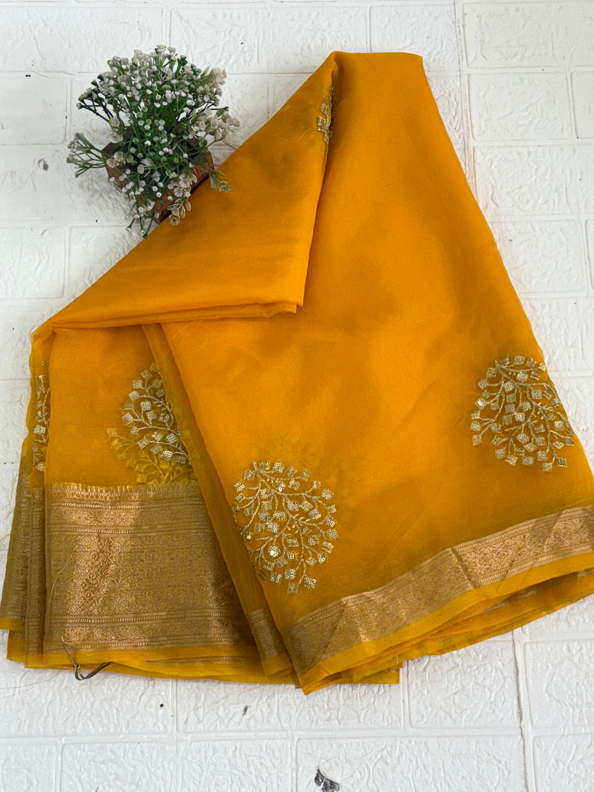 This is likely an Organza or fabric saree. The sheer, light-weight look suggests a fine fabric like Organza, or a similar silk blend, adorned with matching blouse golden zari lines on the pallu and intricate golden sequin or bead floral embroidery