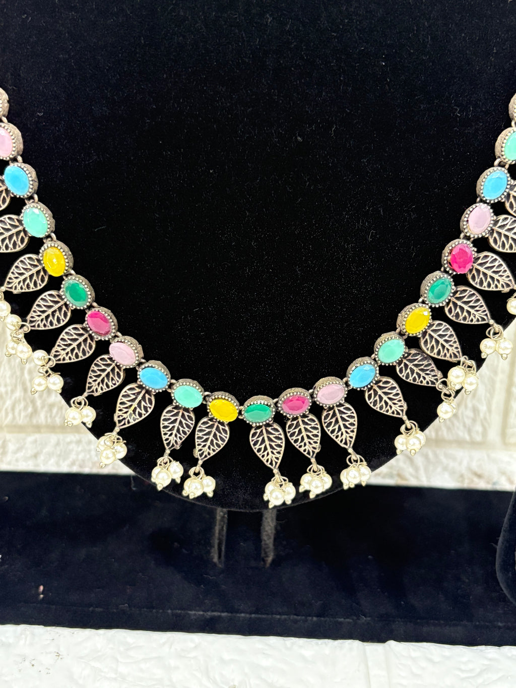 Name:
Colorful Stone Leaf Necklace Set Elegant oxidised silver necklace with multicolor stones, leaf motifs, and pearl drops, paired with matching earrings for a festive ethnic look.