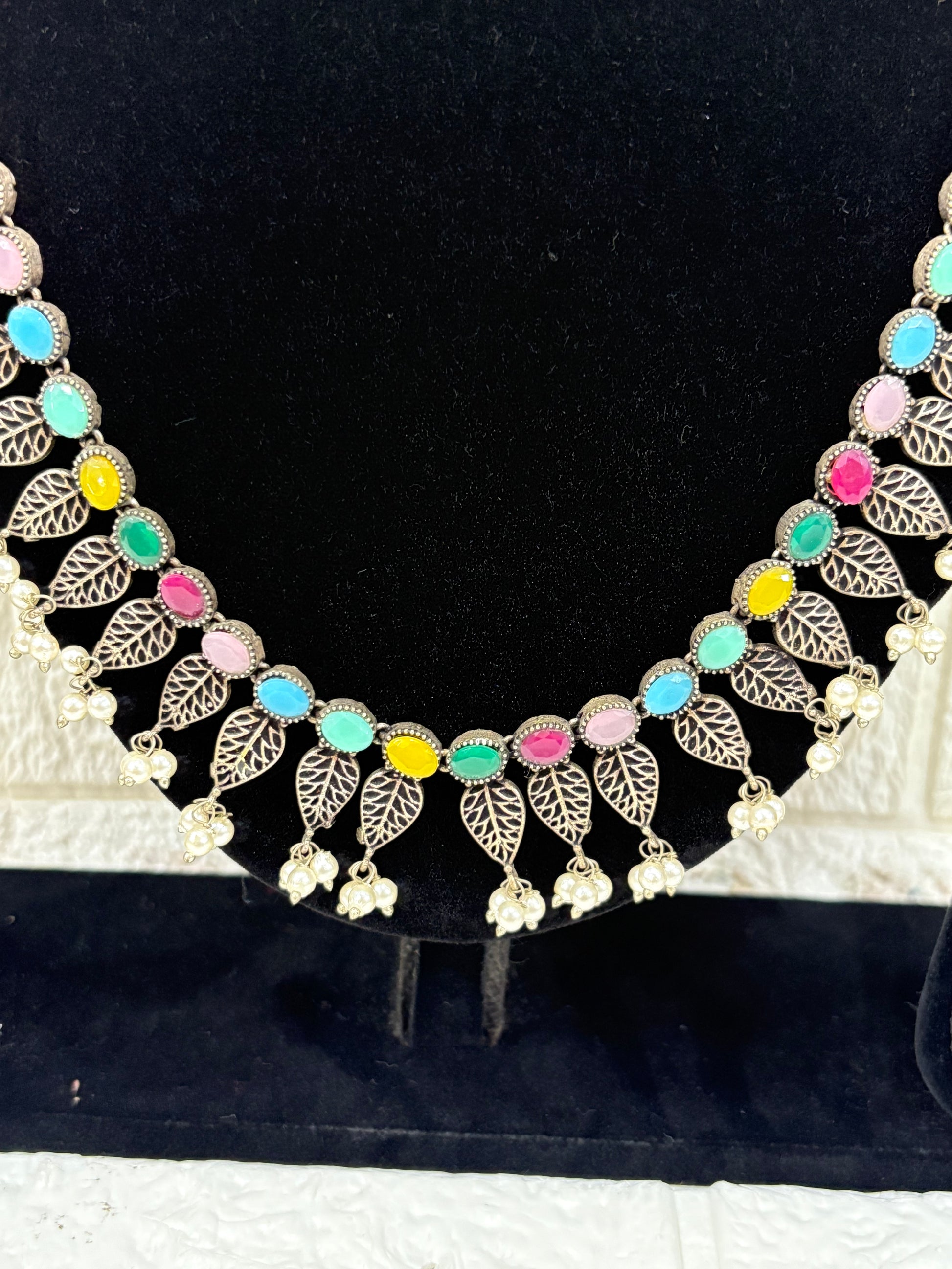 Name:
Colorful Stone Leaf Necklace Set Elegant oxidised silver necklace with multicolor stones, leaf motifs, and pearl drops, paired with matching earrings for a festive ethnic look.