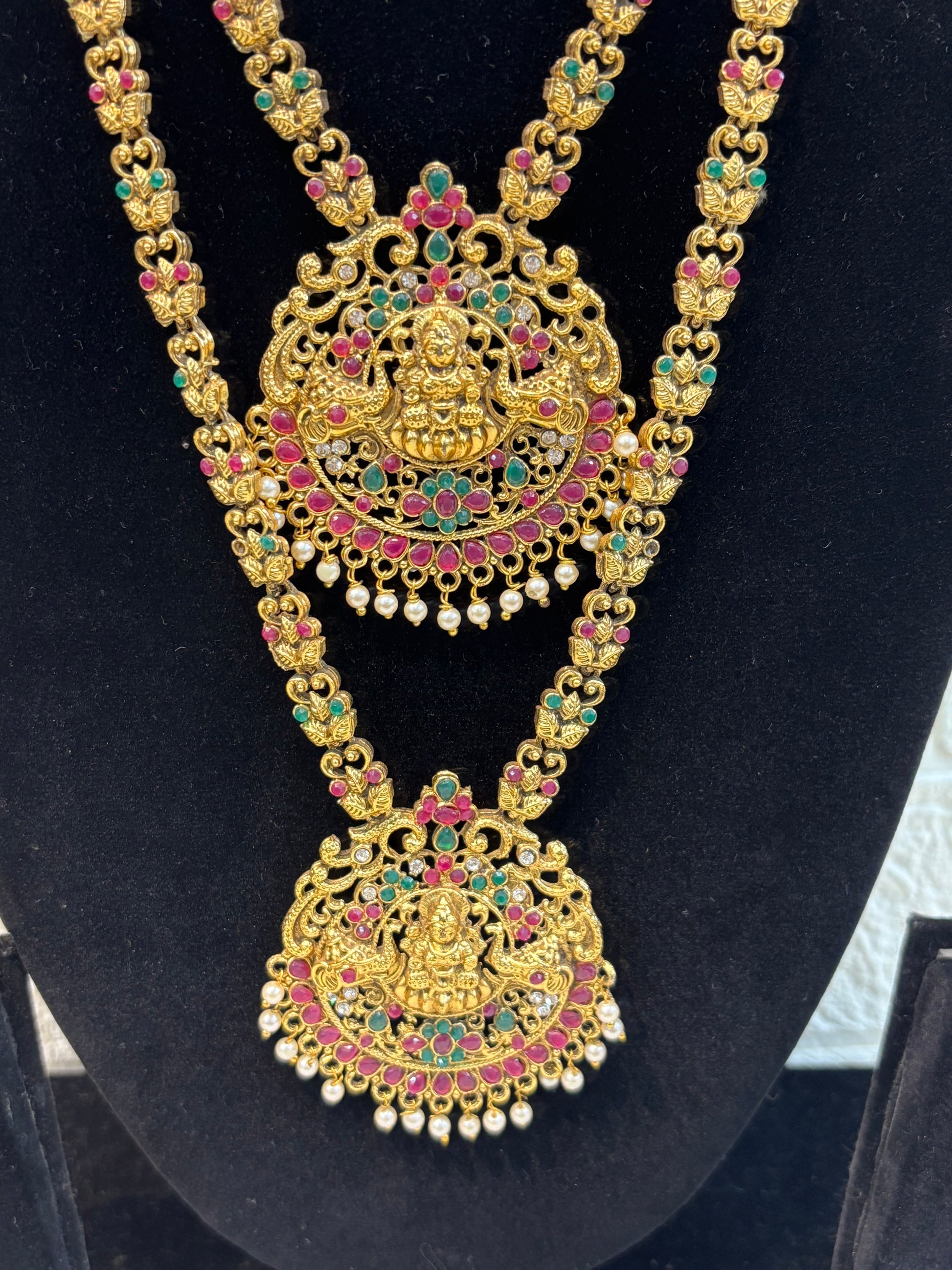 Antique gold-finish temple jewellery featuring intricate Goddess Lakshmi pendants, ruby-green stone detailing, and pearl drops—ideal for weddings and festive w