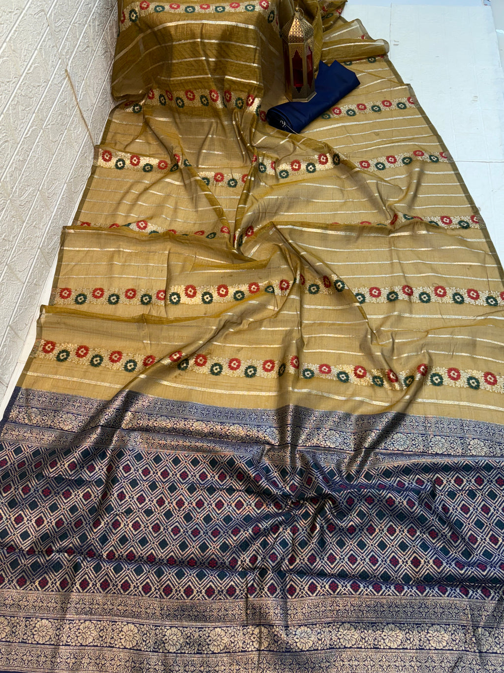 Mustard Bloom Zari Elegant soft cotton saree with fine zari stripes, multicolor floral butti bands, and a richly woven navy-blue zari pallu and border for a traditional festive appeal.