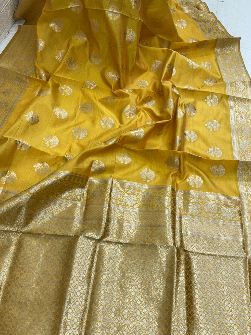 The saree appears to be a Banarasi brocade silk saree it is made of silk with rich zari (metallic thread) brocade weaving characteristic of the Banarasi style from Varanasi India the body features small fish (meen) motifs