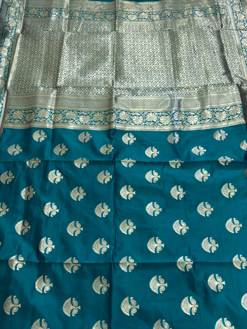 The saree appears to be a Banarasi Brocade Silk Saree.
It is made of silk with rich zari (metallic thread) brocade weaving, characteristic of the Banarasi style from Varanasi, India. The body features small fish (meen) motifs,