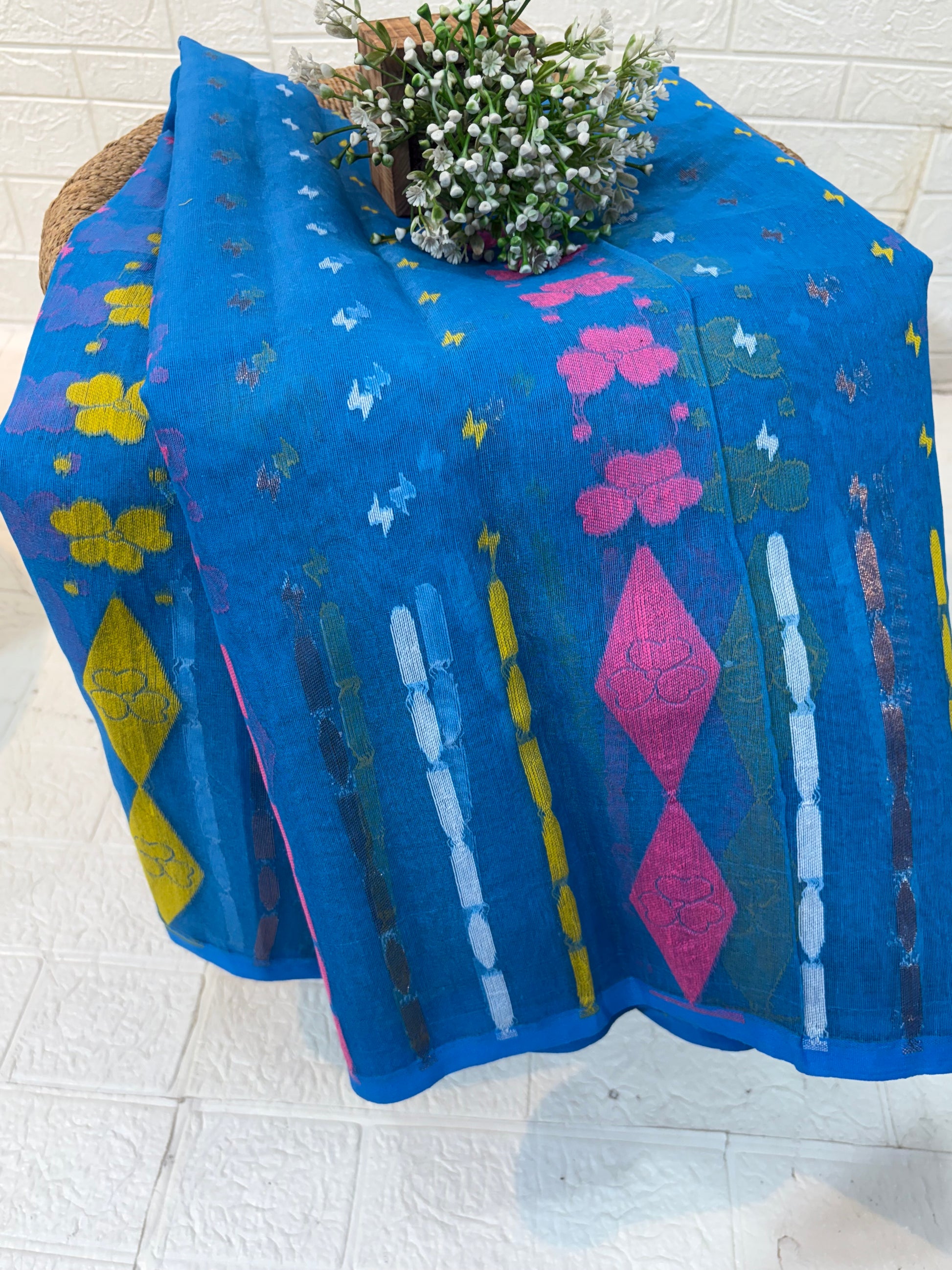 Jamdani Saree Made from airy cotton Jamdani, featuring a soothing blue base with multicolour floral butis and a beautifully woven contrast border for a fresh, elegant appeal.