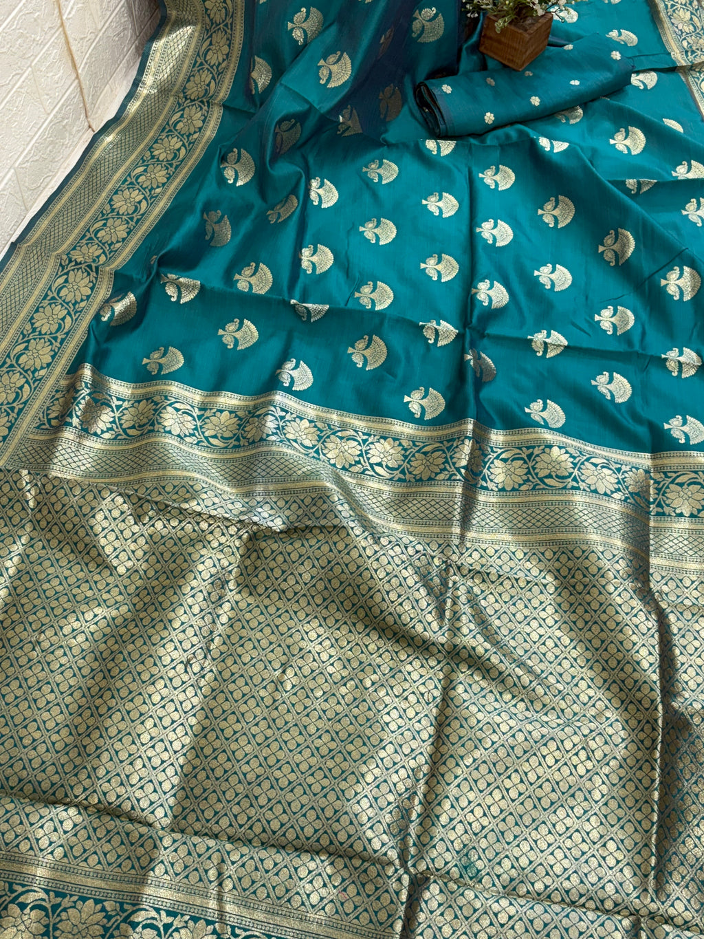 The saree appears to be a Banarasi Brocade Silk Saree.
It is made of silk with rich zari (metallic thread) brocade weaving, characteristic of the Banarasi style from Varanasi, India. The body features small fish (meen) motifs,