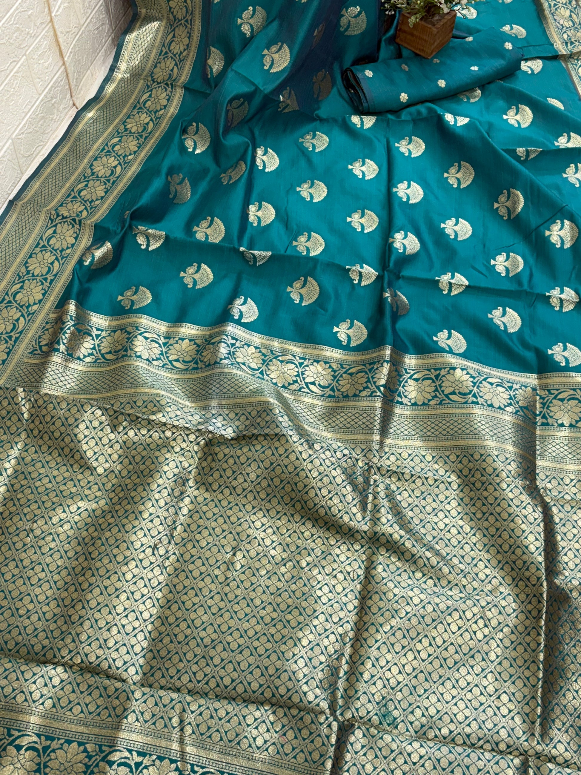 The saree appears to be a Banarasi Brocade Silk Saree.
It is made of silk with rich zari (metallic thread) brocade weaving, characteristic of the Banarasi style from Varanasi, India. The body features small fish (meen) motifs,