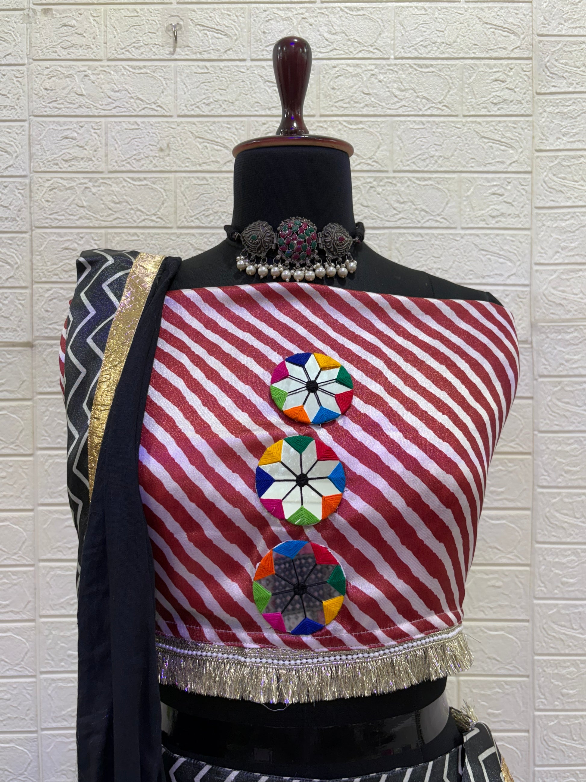 Name: Black & Red Chevron Lehenga set Crafted from soft satin blend with bold chevron print vibrant multicolor tassels, and mirror detailing with mirror work blouse, and black dupatta with gold border – a chic pick for festive and Navratri celebrations.