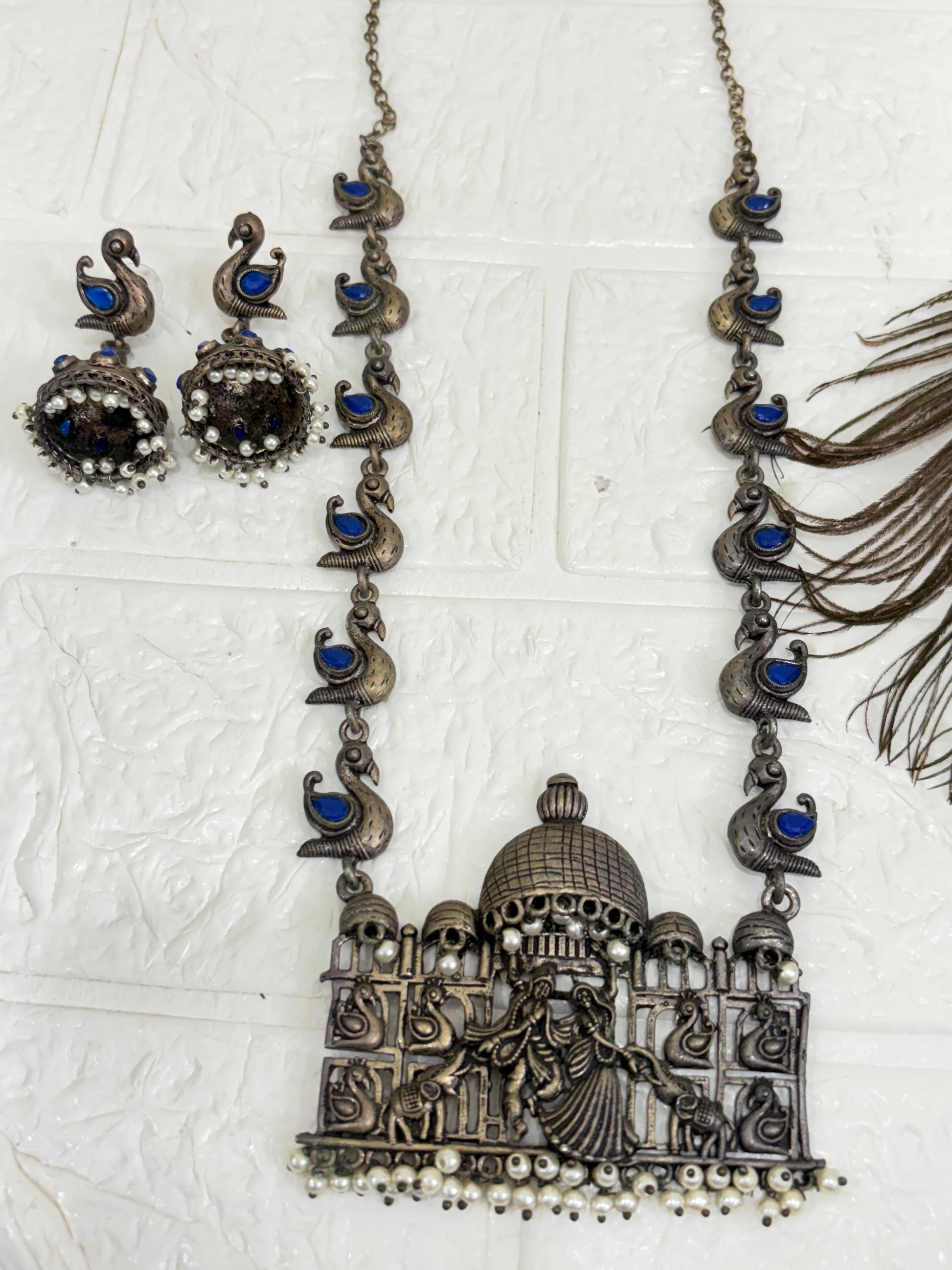 Name:
Heritage Dandiya Dome Necklace Set Oxidised silver necklace with temple-style dome pendant featuring dandiya dance motifs, accented with blue stone paisleys and matching jhumka earrings.