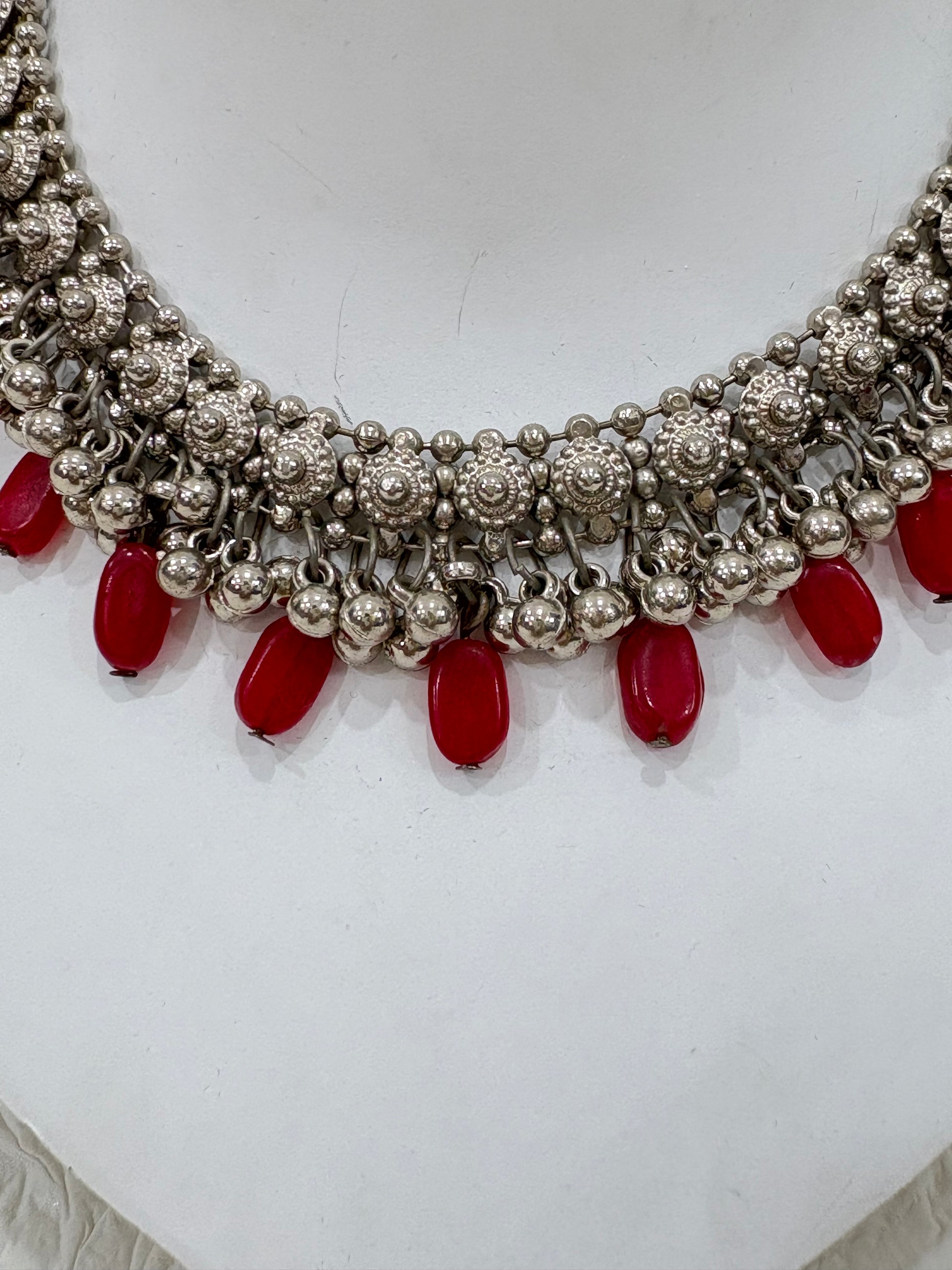 Name:
Oxidised Silver Red Bead Choker Antique-style oxidised choker embellished with intricate floral motifs and bold red bead drops, perfect for festive and wedding wear.