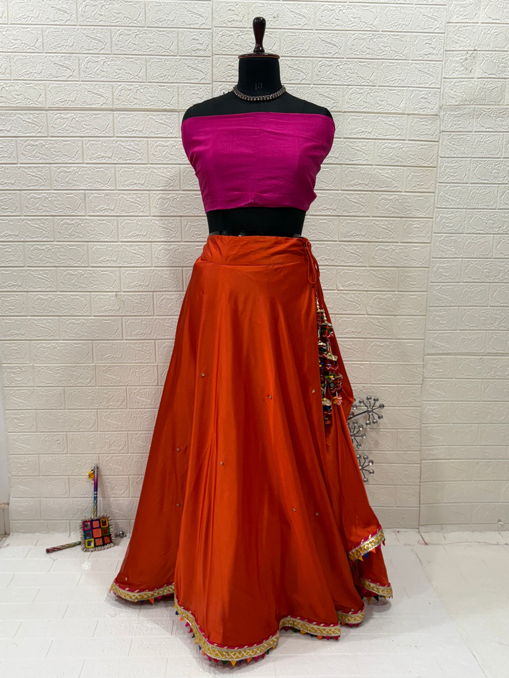 Name: Rust Orange Festive Lehenga Set Crafted soft satin blend with a cotton silk contrast pink blouse and chiffon dupatta, embellished with delicate lace border and subtle mirror work – perfect for festive occasions.