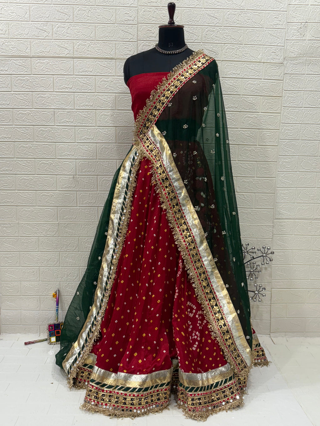Name:
Red & Green Bandhni Lehenga Crafted in soft pure synthetic satin Bandhani print traditional paired with intricate gota-patti work, paired with a Bottle Green Organza dupatta embellished with mirror and zari lace for a festive, royal look.