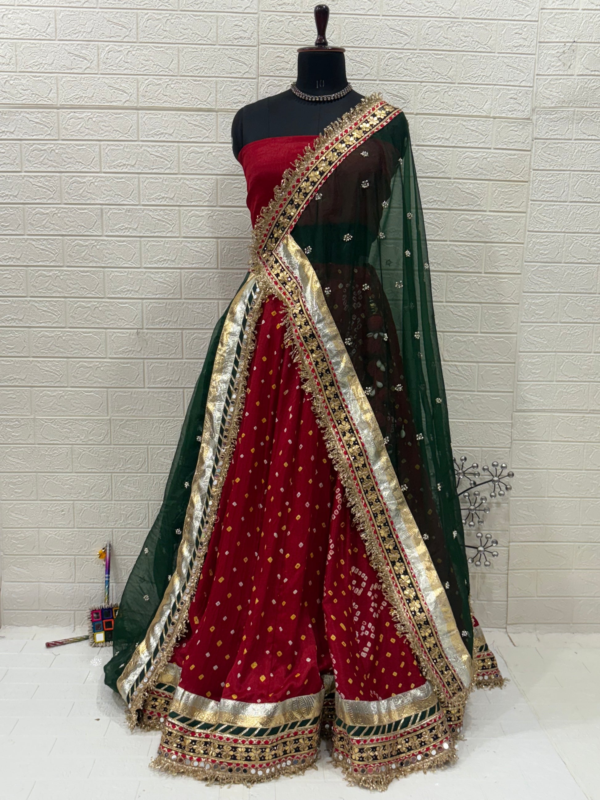 Name:
Red & Green Bandhni Lehenga Crafted in soft pure synthetic satin Bandhani print traditional paired with intricate gota-patti work, paired with a Bottle Green Organza dupatta embellished with mirror and zari lace for a festive, royal look.
