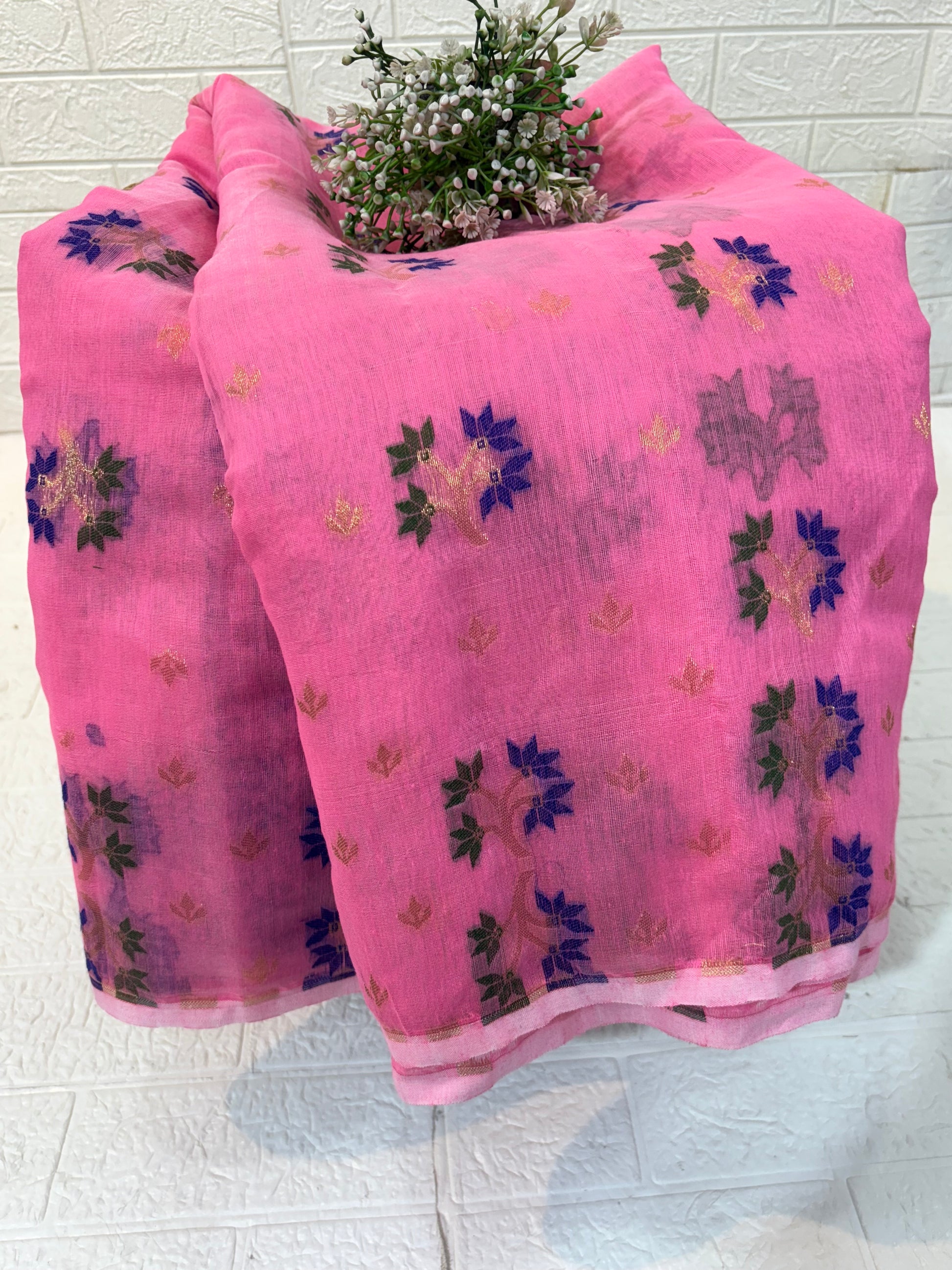 Jamdani Saree Crafted in soft, cotton Jamdani, featuring a delicate pink base with multicolour floral butis and a richly woven ornamental border for an elegant festive look.