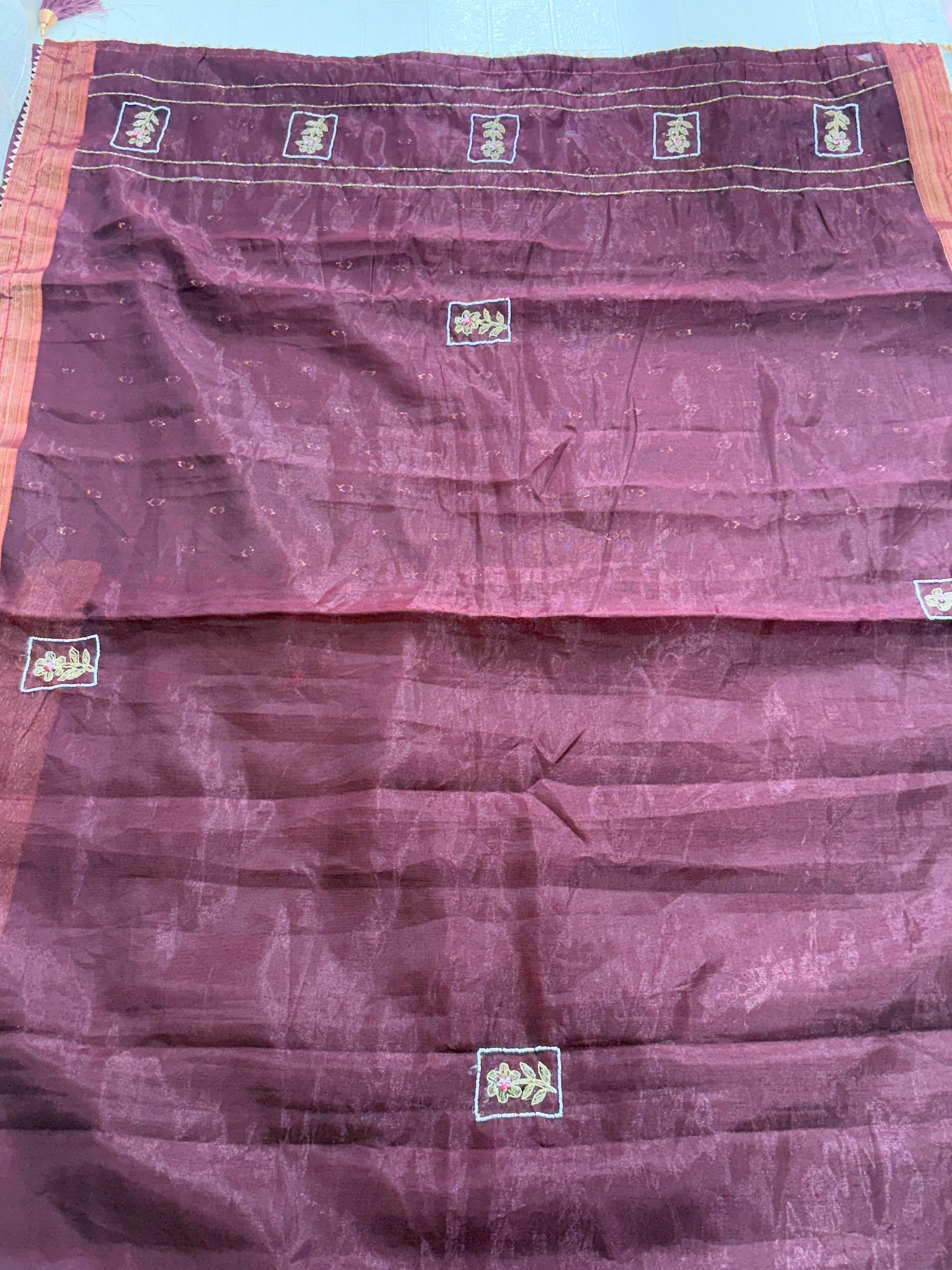 Name: Chanderi or Cotton Silk Saree Fabric The fine texture, sheen, and way the material is folded suggest a Chanderi or Cotton Silk Blend. The work is Zari Woven Stripes with Aari/Thread Embroidery motifs.