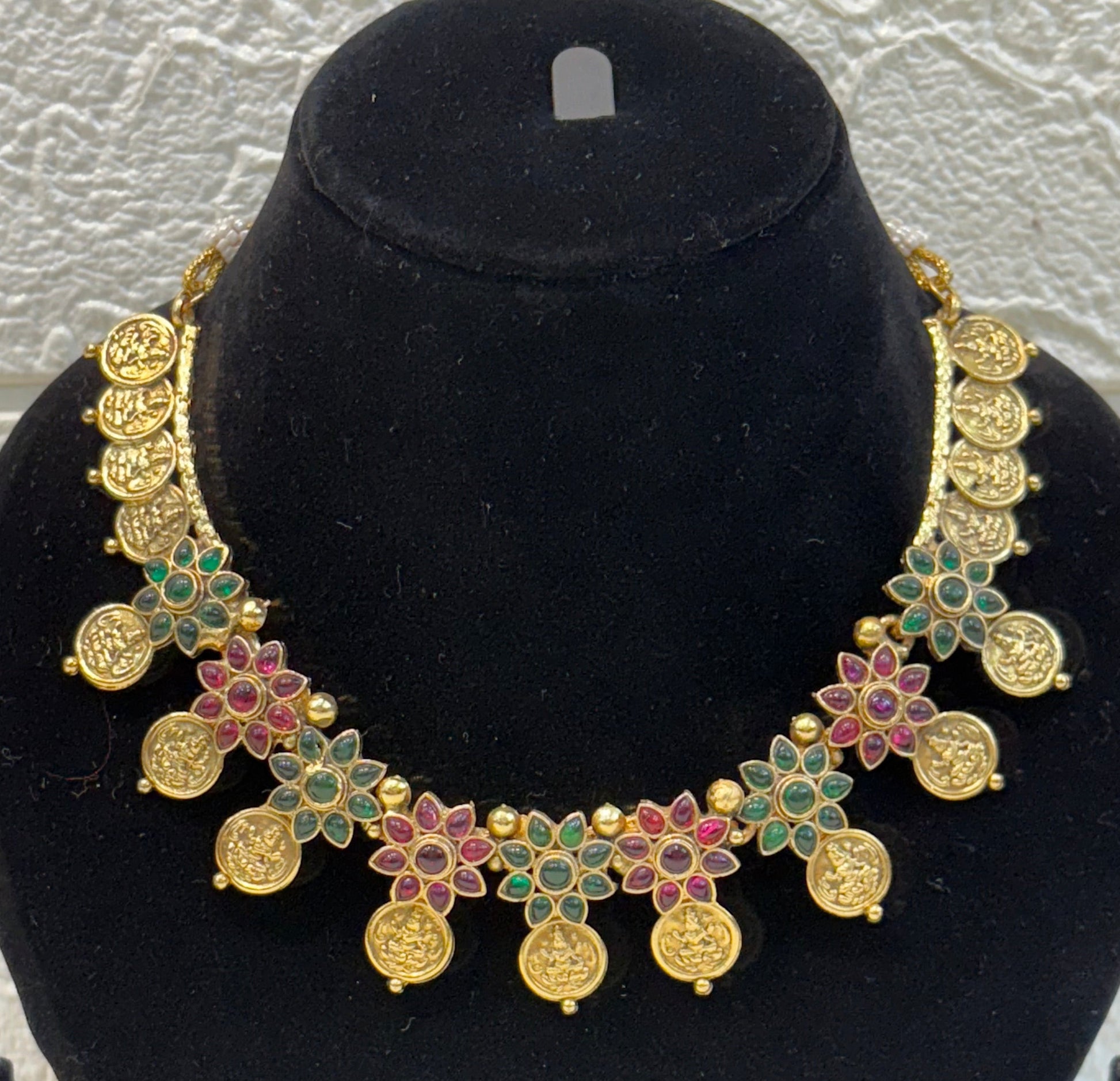 Traditional antique-finish necklace adorned with coin motifs, ruby-green floral stone work, and matching earrings—perfect for festive and wedding occasions.