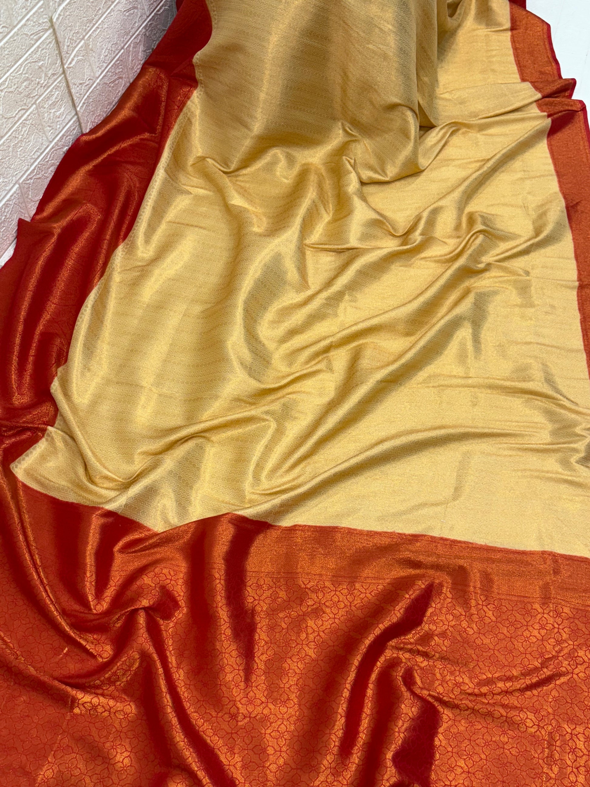 Dual-Tone Rust/Orange Saree kanchipuram silk Fabric A flowing fabric with a lustrous dual-tone (shot) effect, appearing to shift between rust/orange and gold, featuring subtle woven floral buttas/brocade work.