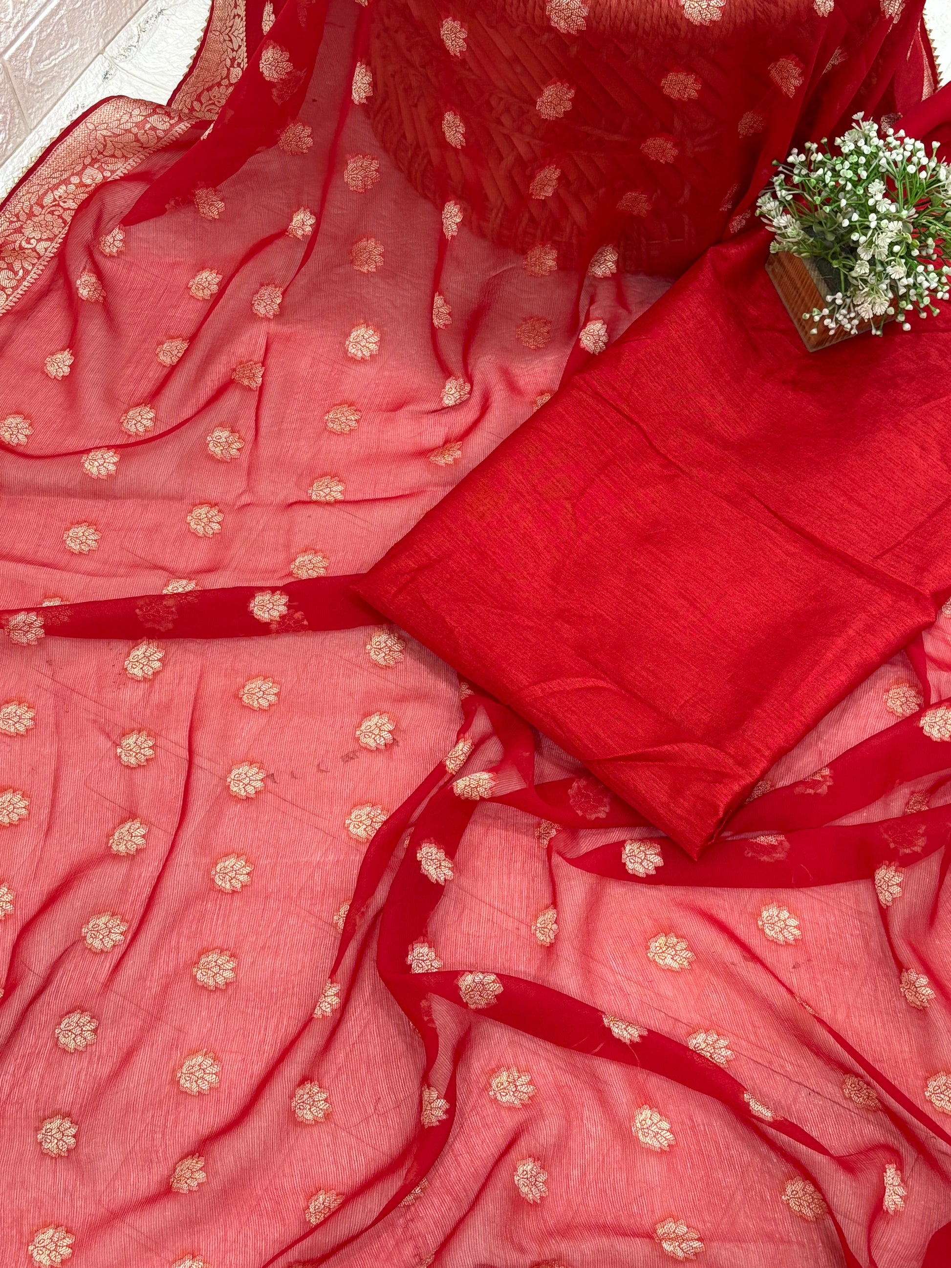 This fabric is a red Georgette with all-over gold zari floral buti embroidery and a rich woven border, paired with a matching plain blouse perfect for festival