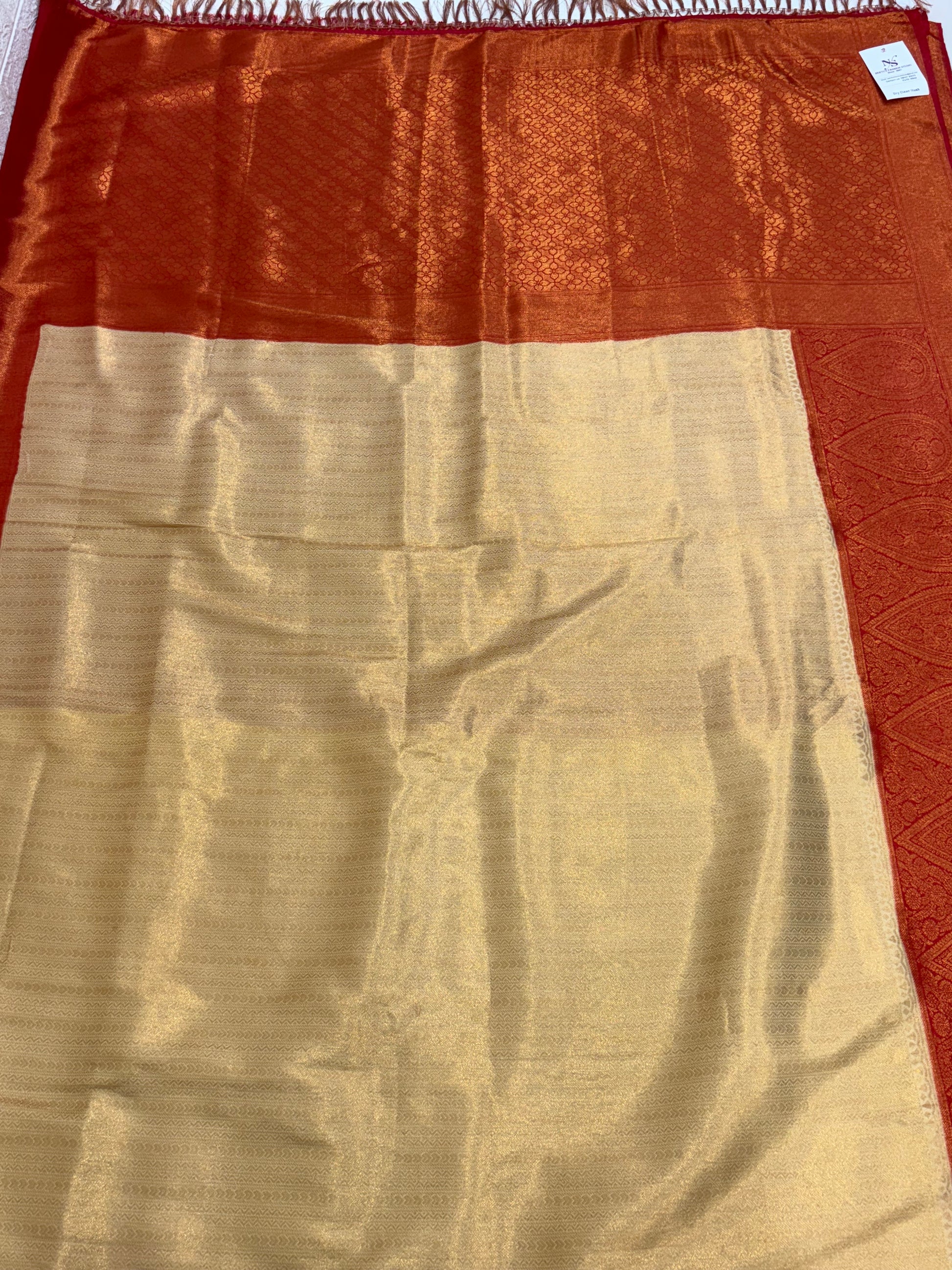 Dual-Tone Rust/Orange Saree kanchipuram silk Fabric A flowing fabric with a lustrous dual-tone (shot) effect, appearing to shift between rust/orange and gold, featuring subtle woven floral buttas/brocade work.