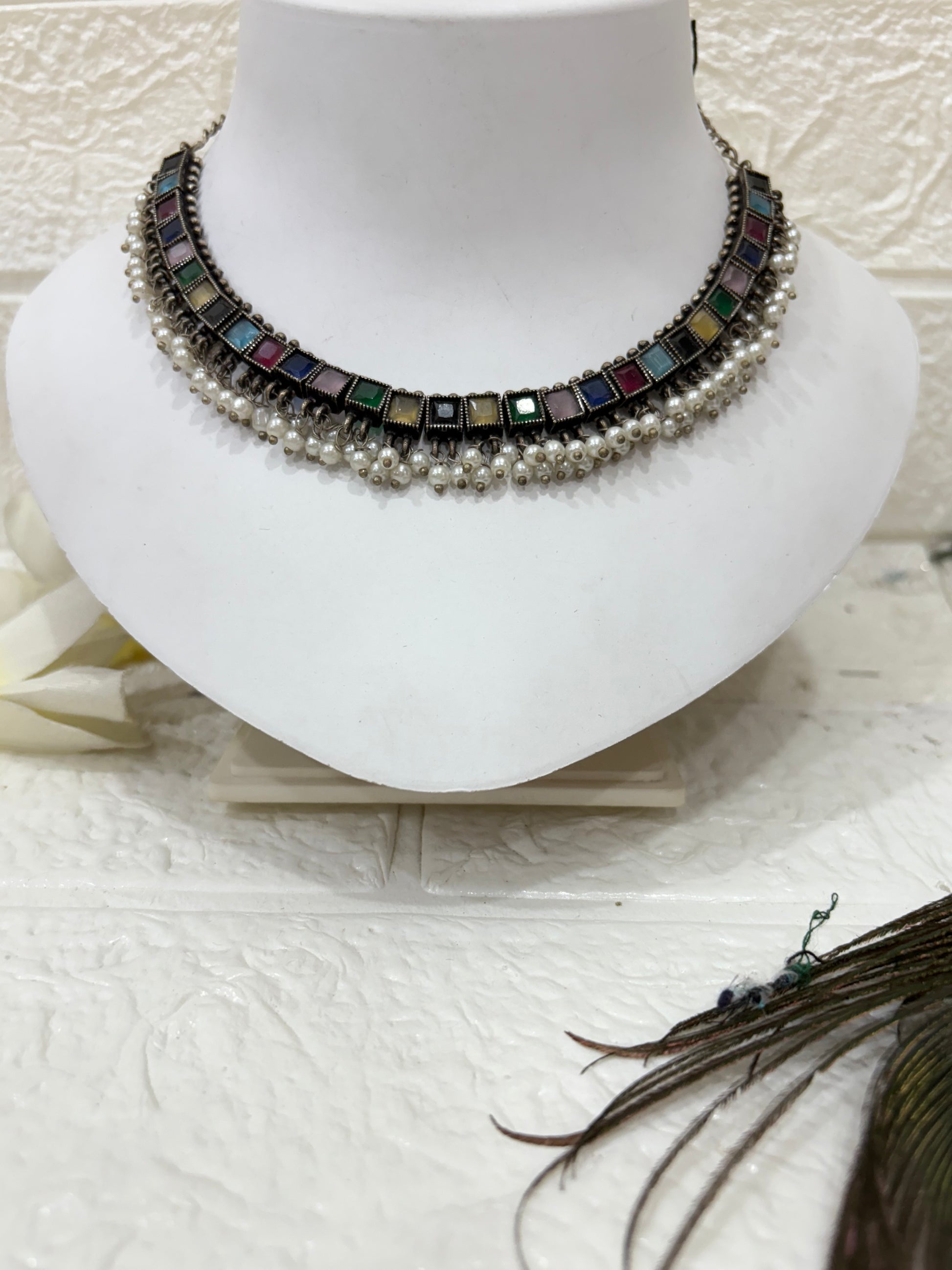 NAME: Boho Mirror Pearl Choker Set Oxidised silver choker adorned with multicolour square stones and pearl drops, paired with matching earrings. Ideal for festive and traditional looks.