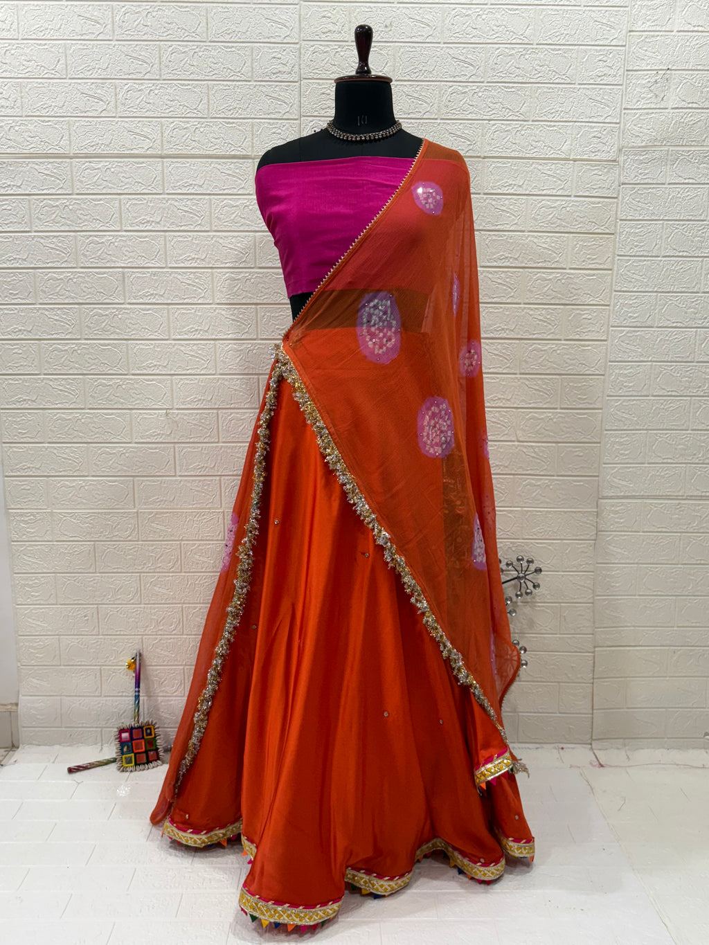 Name: Rust Orange Festive Lehenga Set Crafted soft satin blend with a cotton silk contrast pink blouse and chiffon dupatta, embellished with delicate lace border and subtle mirror work – perfect for festive occasions.