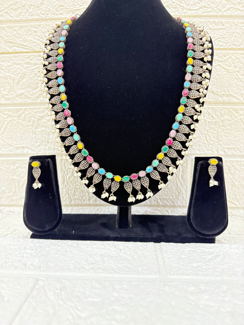 Name:
Colorful Stone Leaf Necklace Set Elegant oxidised silver necklace with multicolor stones, leaf motifs, and pearl drops, paired with matching earrings for a festive ethnic look.
