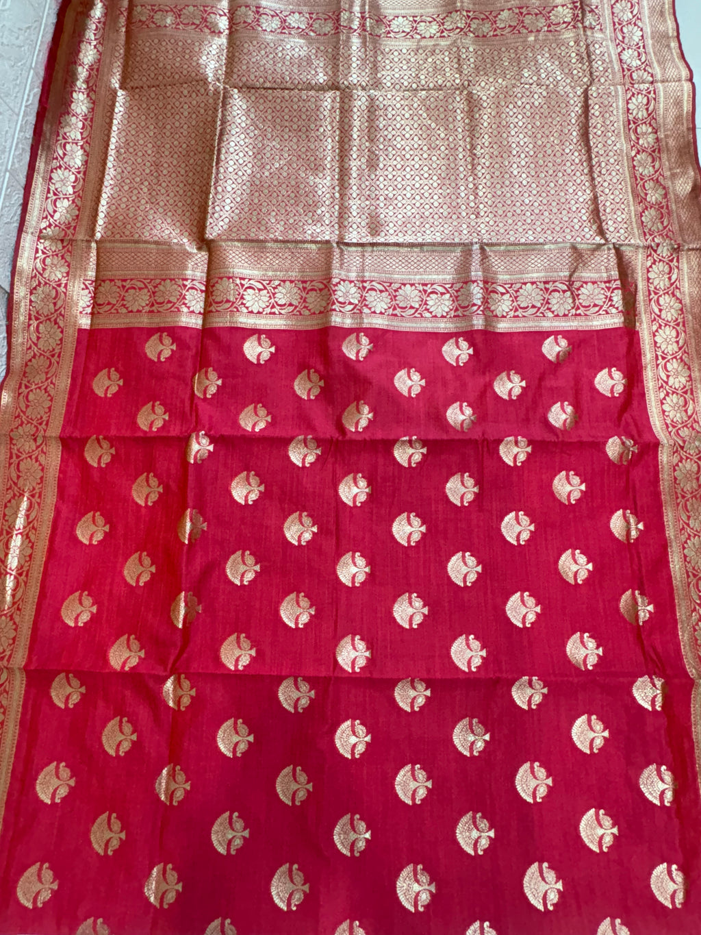 Name: Ruby Bloom Banarasi silk saree A rich ruby red Banarasi silk saree featuring intricate golden zari motifs with floral and lattice border detailing, adding a timeless traditional elegance to any ensemble.