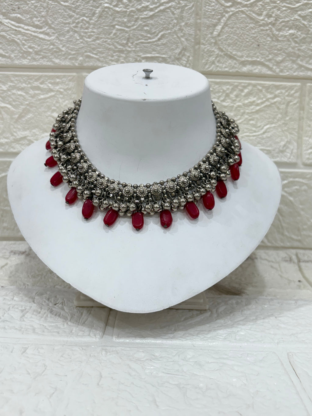 Name:
Oxidised Silver Red Bead Choker Antique-style oxidised choker embellished with intricate floral motifs and bold red bead drops, perfect for festive and wedding wear.