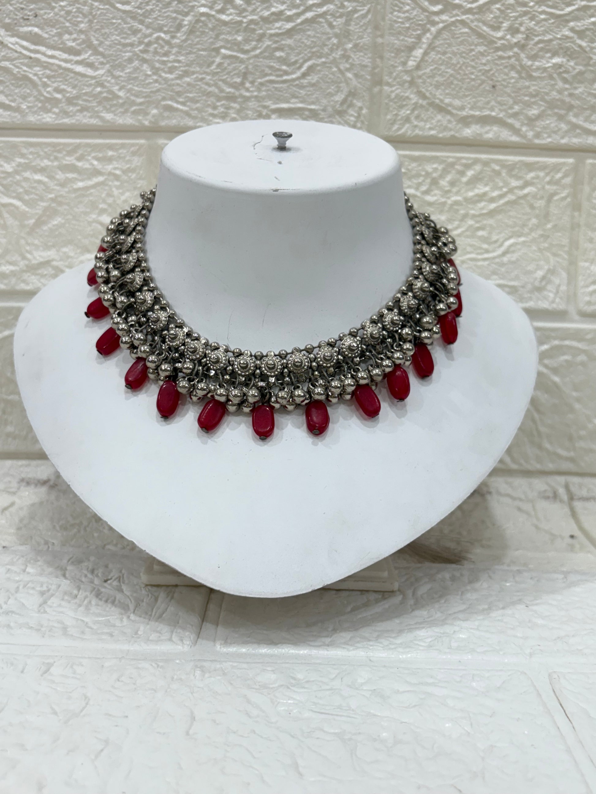 Name:
Oxidised Silver Red Bead Choker Antique-style oxidised choker embellished with intricate floral motifs and bold red bead drops, perfect for festive and wedding wear.
