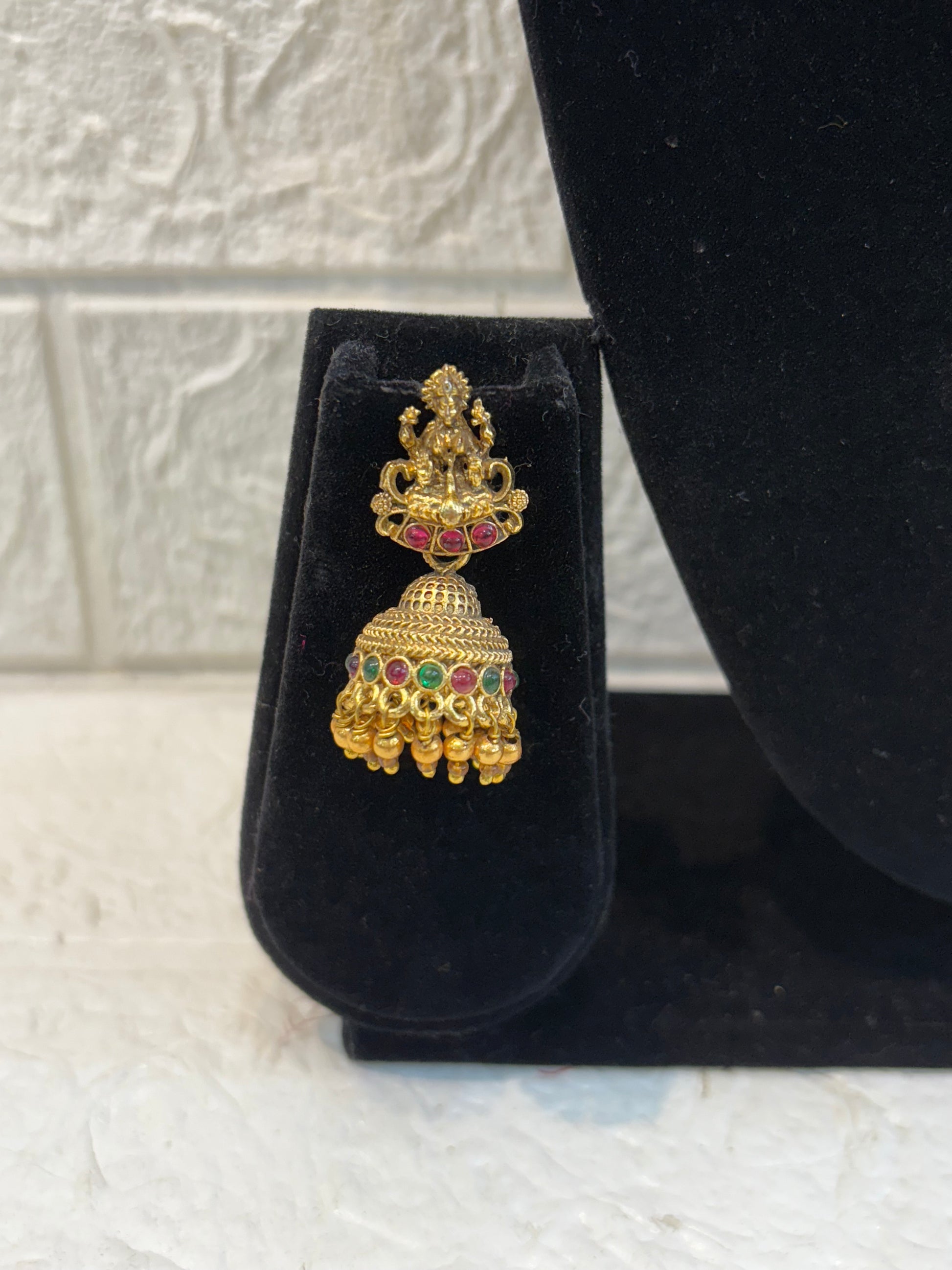 Elegant long haram featuring twin coin-style pendants with intricate embossing, ruby-green stone chain work, and traditional jhumka earrings—perfect for bridal and festive wear.