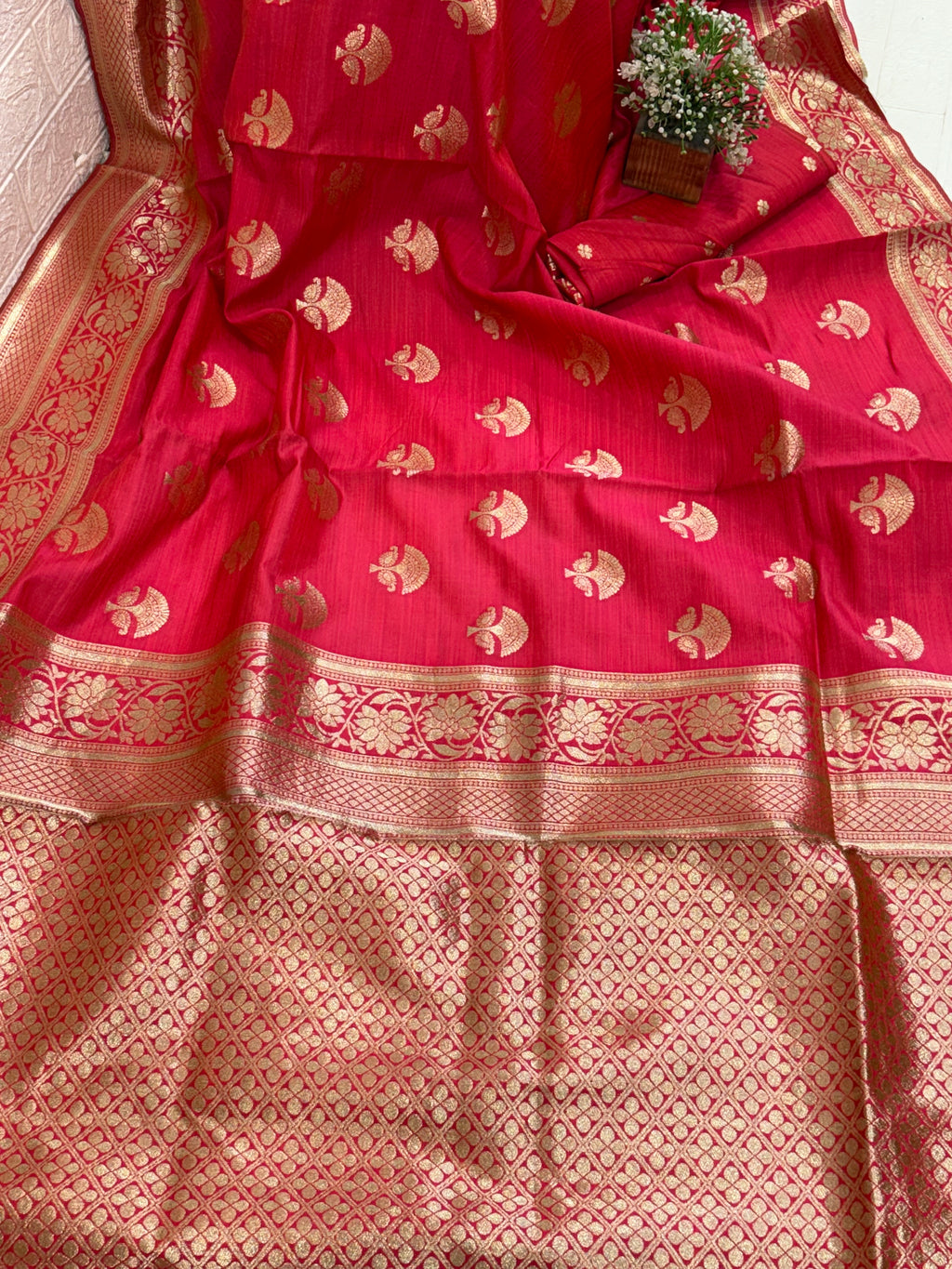 Name: Ruby Bloom Banarasi silk saree A rich ruby red Banarasi silk saree featuring intricate golden zari motifs with floral and lattice border detailing, adding a timeless traditional elegance to any ensemble.