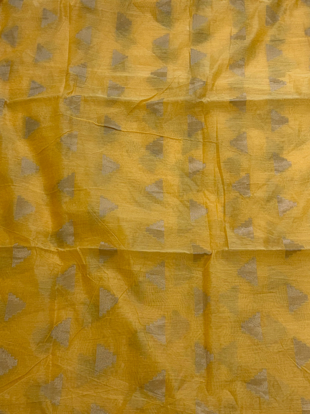 The saree is most likely cotton silk a blend like  The lightweight, sheer nature of the yellow fabric, adorned with all-over gold zari woven triangular motifs, is characteristic of these silks. The geometric patte