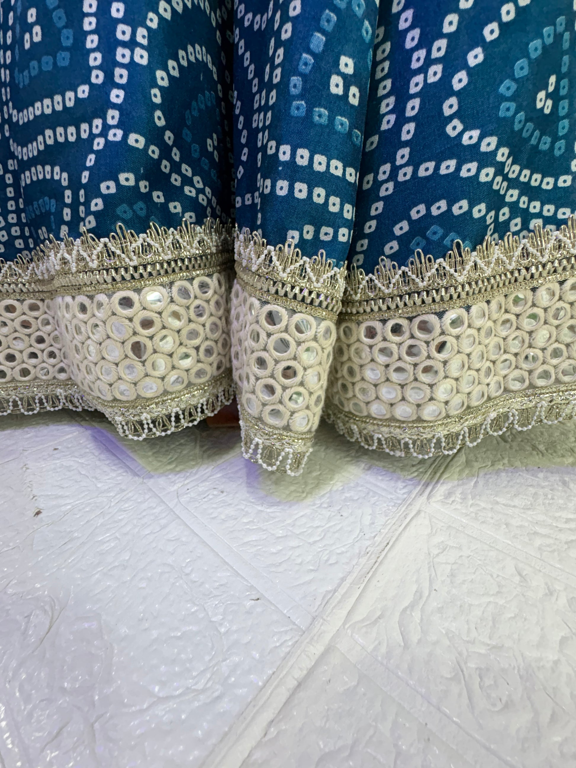 Name:  Blue Bandhani  Lehenga Set Made from soft cotton  Bandhani  print fabric with a mirror work border and paired with a chiffon white dupatta – perfect for festive and traditional celebrations.