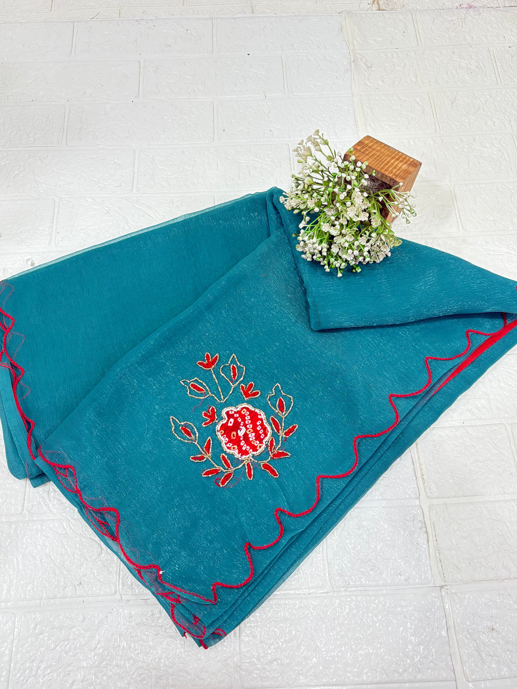 lightweight Teal Shimmer Organza with Embroidered material in a teal shade. It has a sheer, slightly shimmery texture with delicate embroidered floral motifs in red and gold scattered across the fabric. The border is finished with a fine red edg
