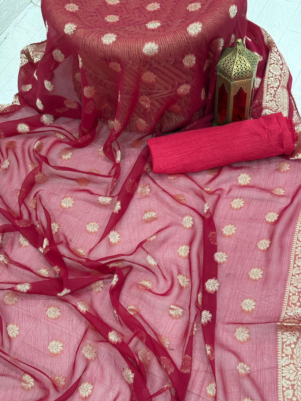 This fabric is a maroon soft Georgette with all over gold zari floral buti embroider and a rich woven border paired with a matching plain blouse perfect for festival