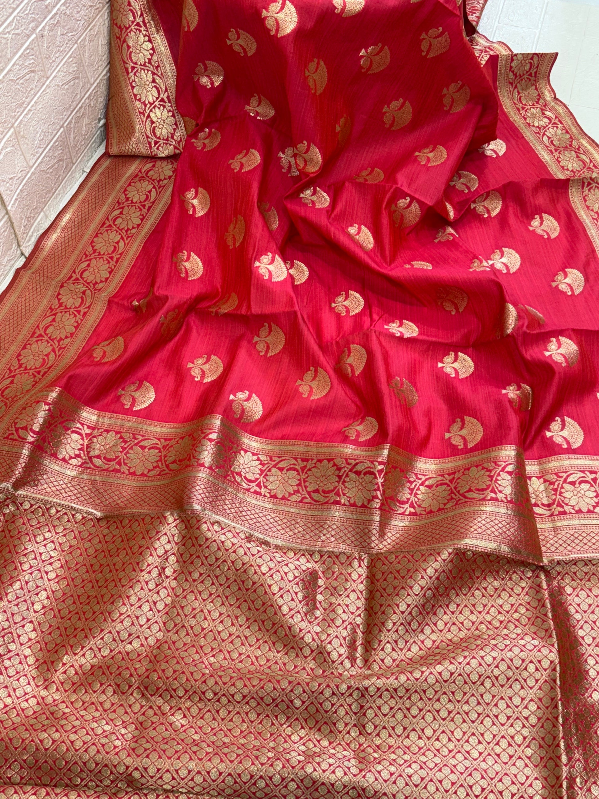 Name: Ruby Bloom Banarasi silk saree A rich ruby red Banarasi silk saree featuring intricate golden zari motifs with floral and lattice border detailing, adding a timeless traditional elegance to any ensemble.