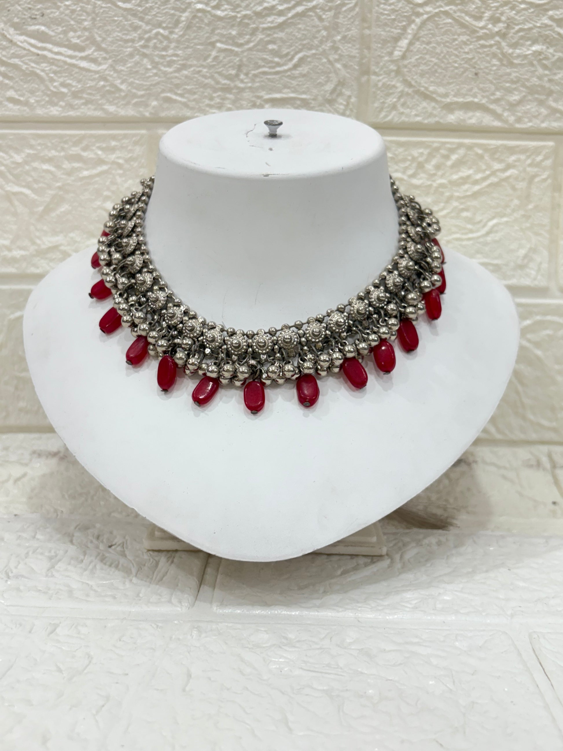Name:
Oxidised Silver Red Bead Choker Antique-style oxidised choker embellished with intricate floral motifs and bold red bead drops, perfect for festive and wedding wear.