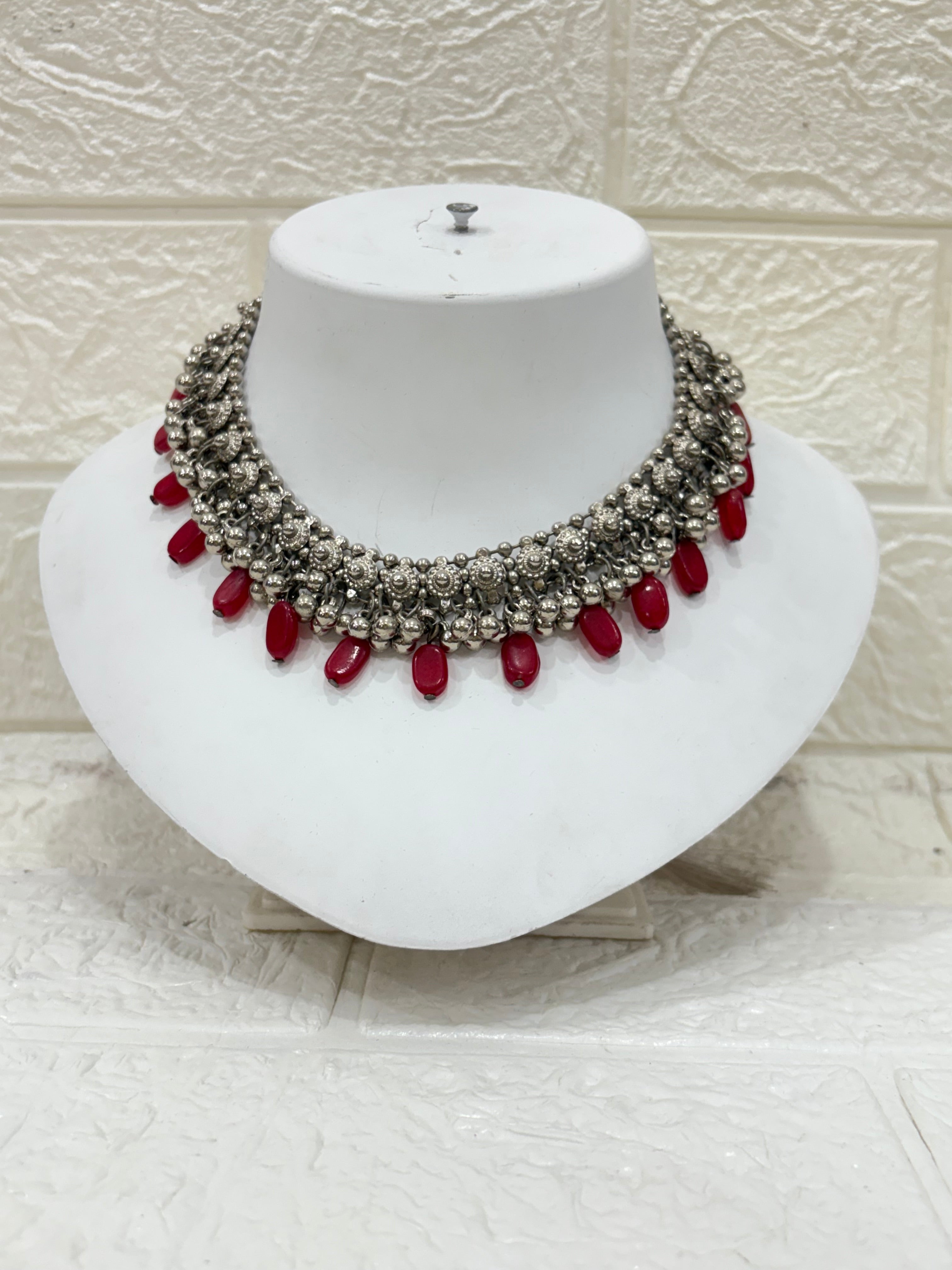 Name:
Oxidised Silver Red Bead Choker Antique-style oxidised choker embellished with intricate floral motifs and bold red bead drops, perfect for festive and wedding wear.
