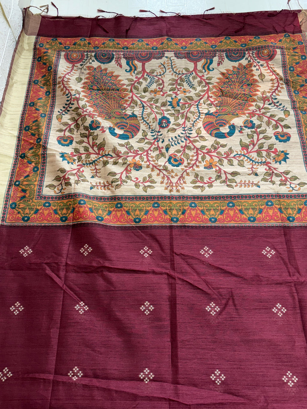 Fabric: Likely Art Silk, The body has a slub/raw silk texture (Maroon/Burgundy), and the pallu features a detailed, nature-inspired design with peacock motifs, which is characteristic of Kalamkari art.