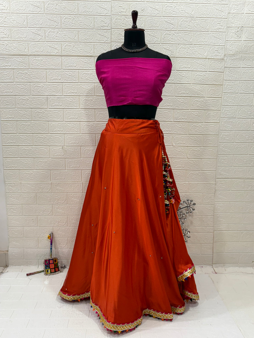 Name: Rust Orange Festive Lehenga Set Crafted soft satin blend with a cotton silk contrast pink blouse and chiffon dupatta, embellished with delicate lace border and subtle mirror work – perfect for festive occasions.